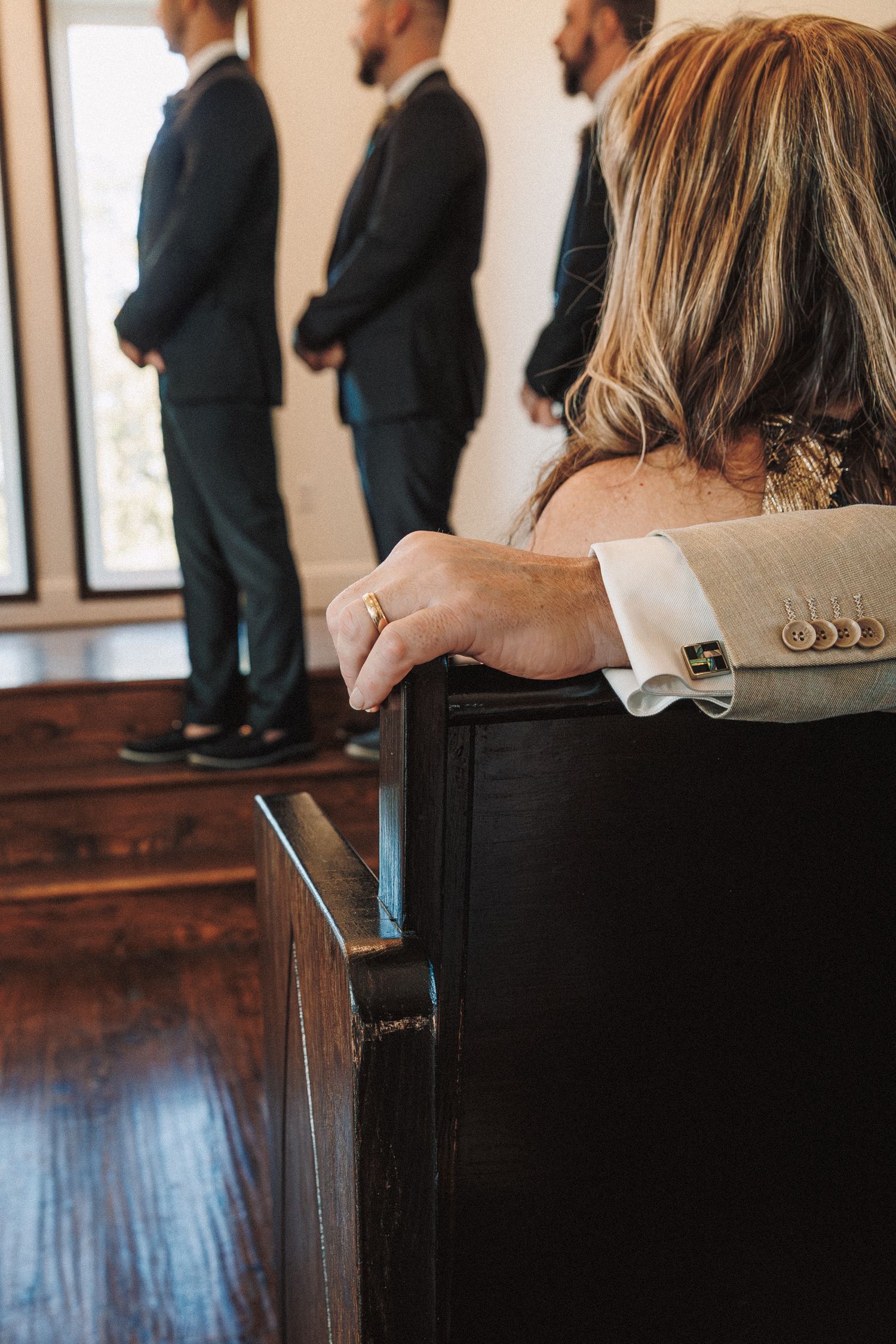 Wedding guest seated on wooden pew watching groomsmen stand at altar during ceremony.