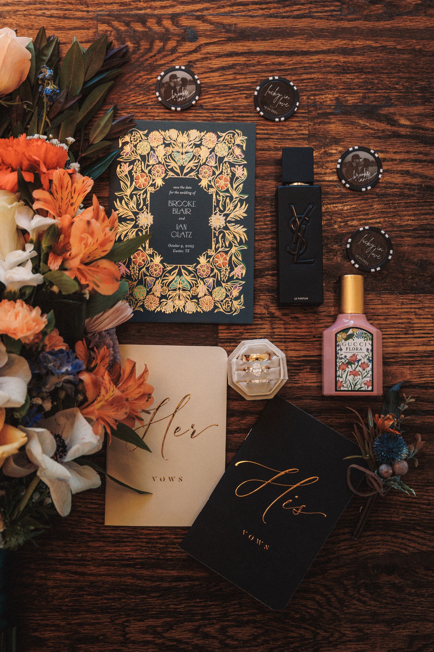 Elegant wedding flat lay featuring floral invitations, YSL and Gucci perfumes, a diamond ring, and His and Her vow books.