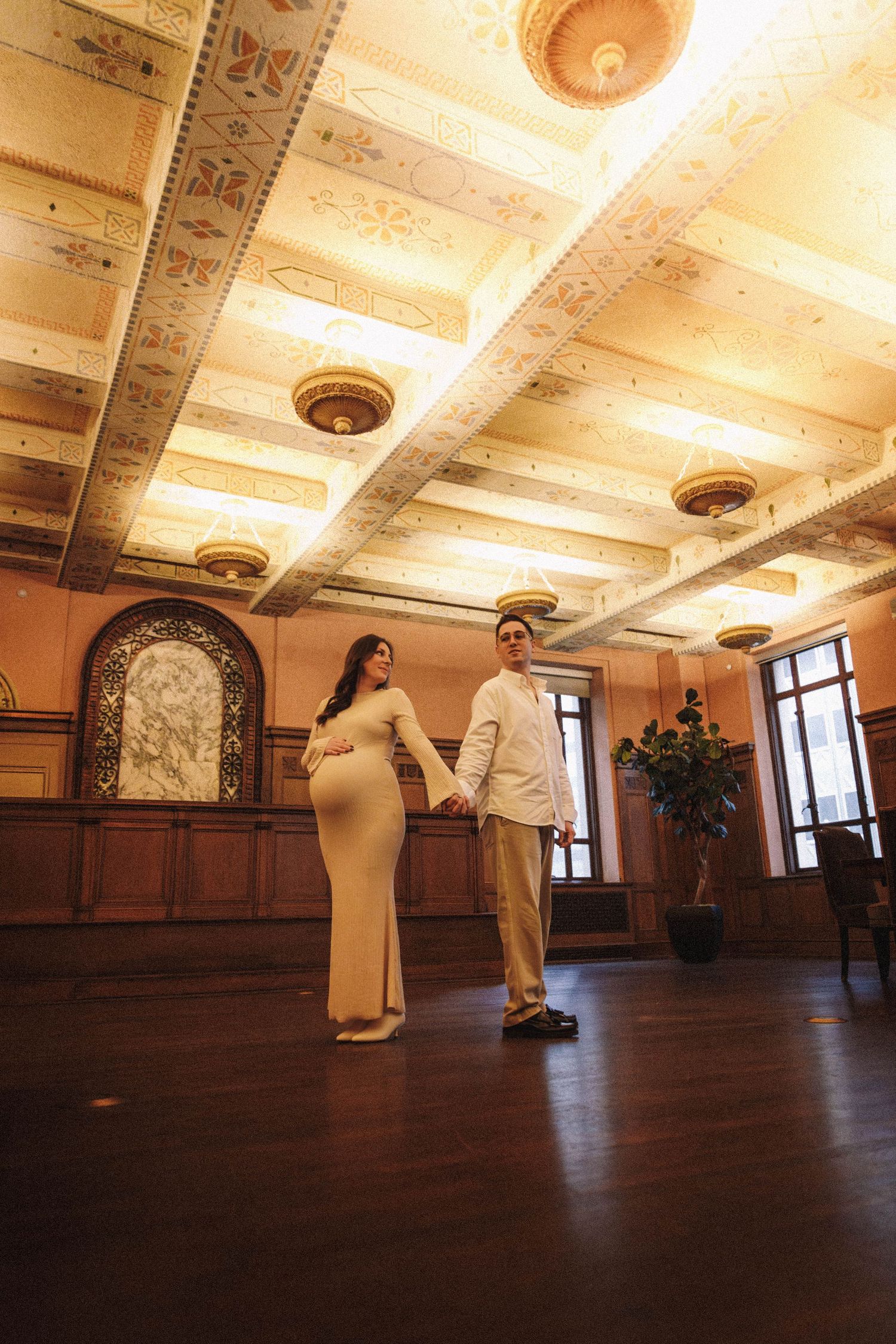 People in white robes practicing Tai Chi movements in an ornate room with a decorative carved ceiling.