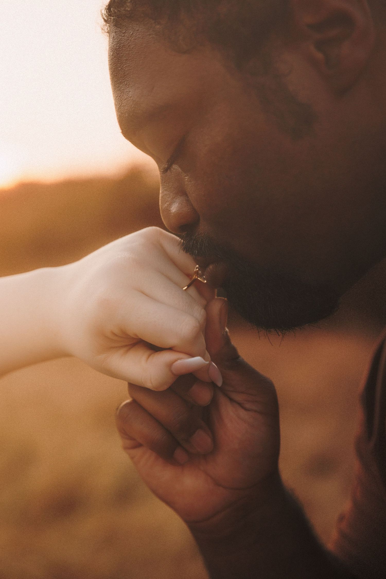 A tender moment captured in warm light showing a gentle kiss on fingers during an intimate photoshoot.