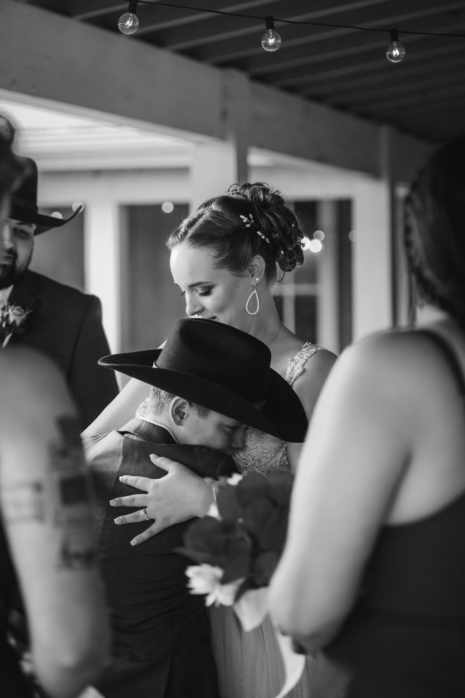 Black and white candid photograph showing an intimate moment of embracing and dancing at an indoor event.