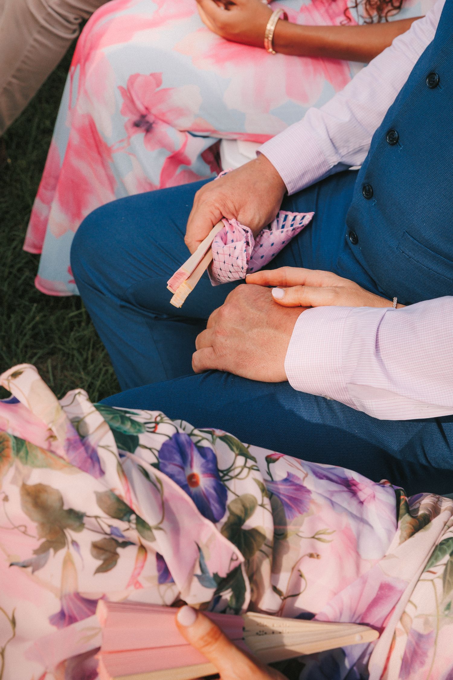 Close-up detail of floral dress fabric and blue suit at outdoor wedding.