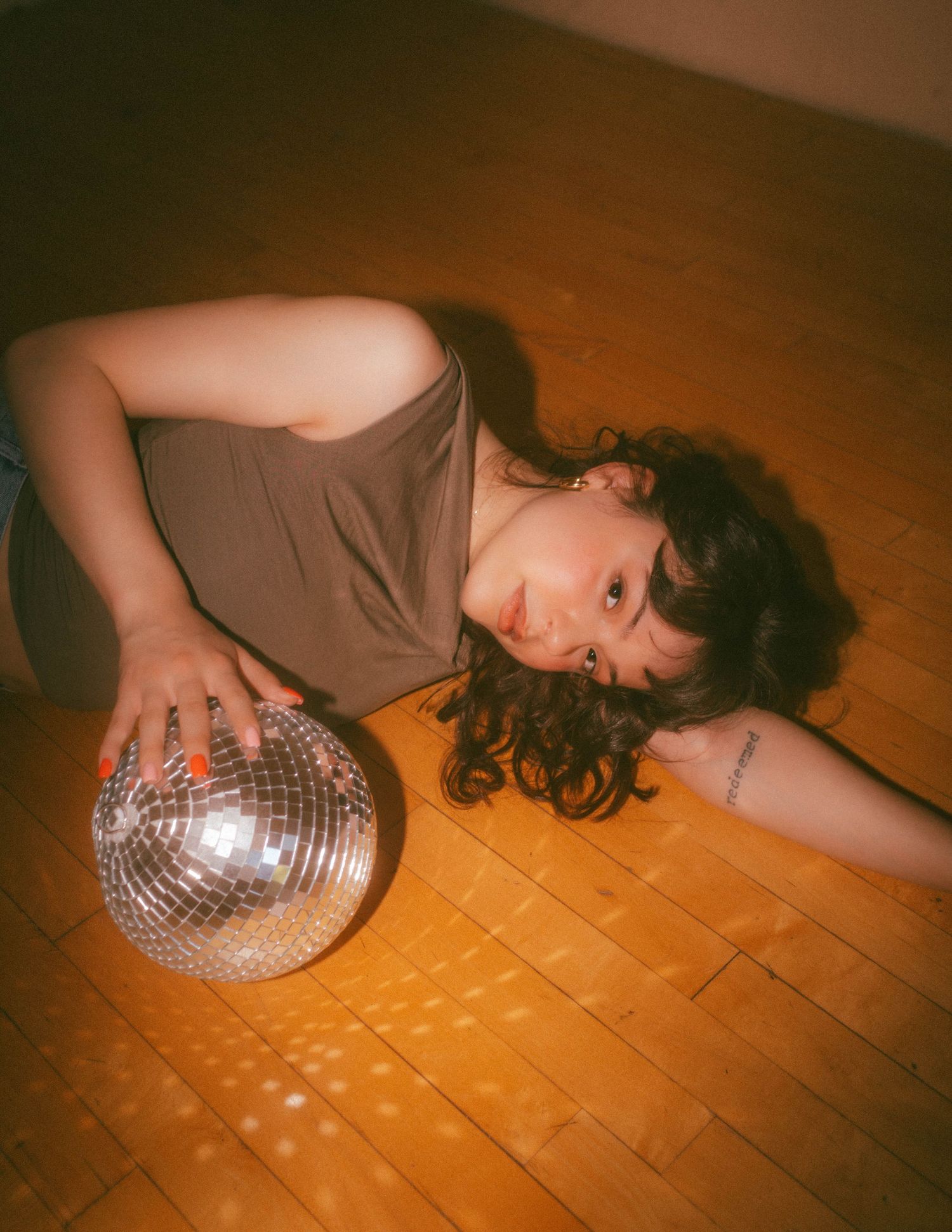A composite image showing a person lying on a wooden floor next to a disco ball, creating a moody nightclub atmosphere.