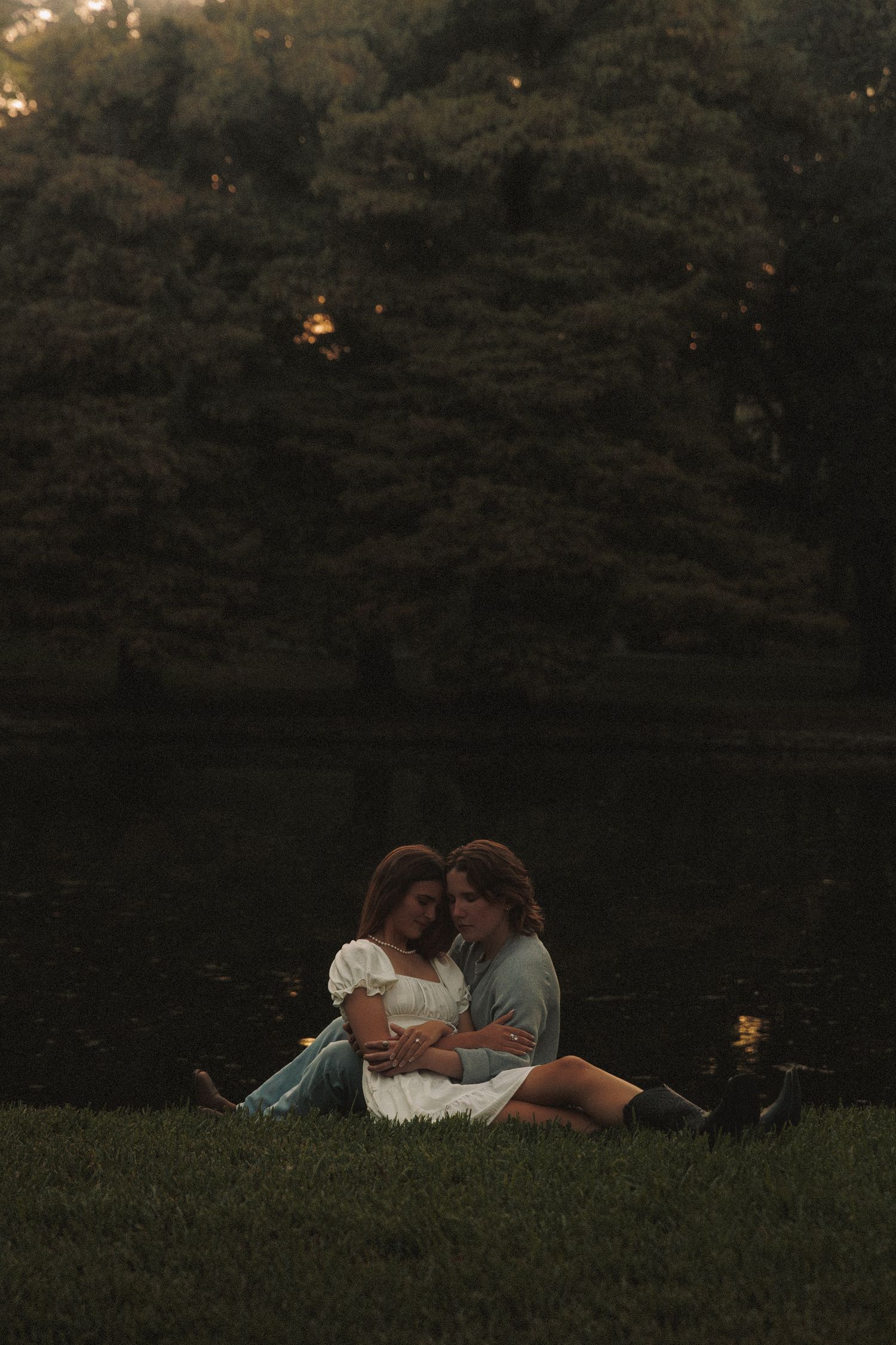 Couple relaxing together on grassy hillside at dusk in romantic outdoor setting.