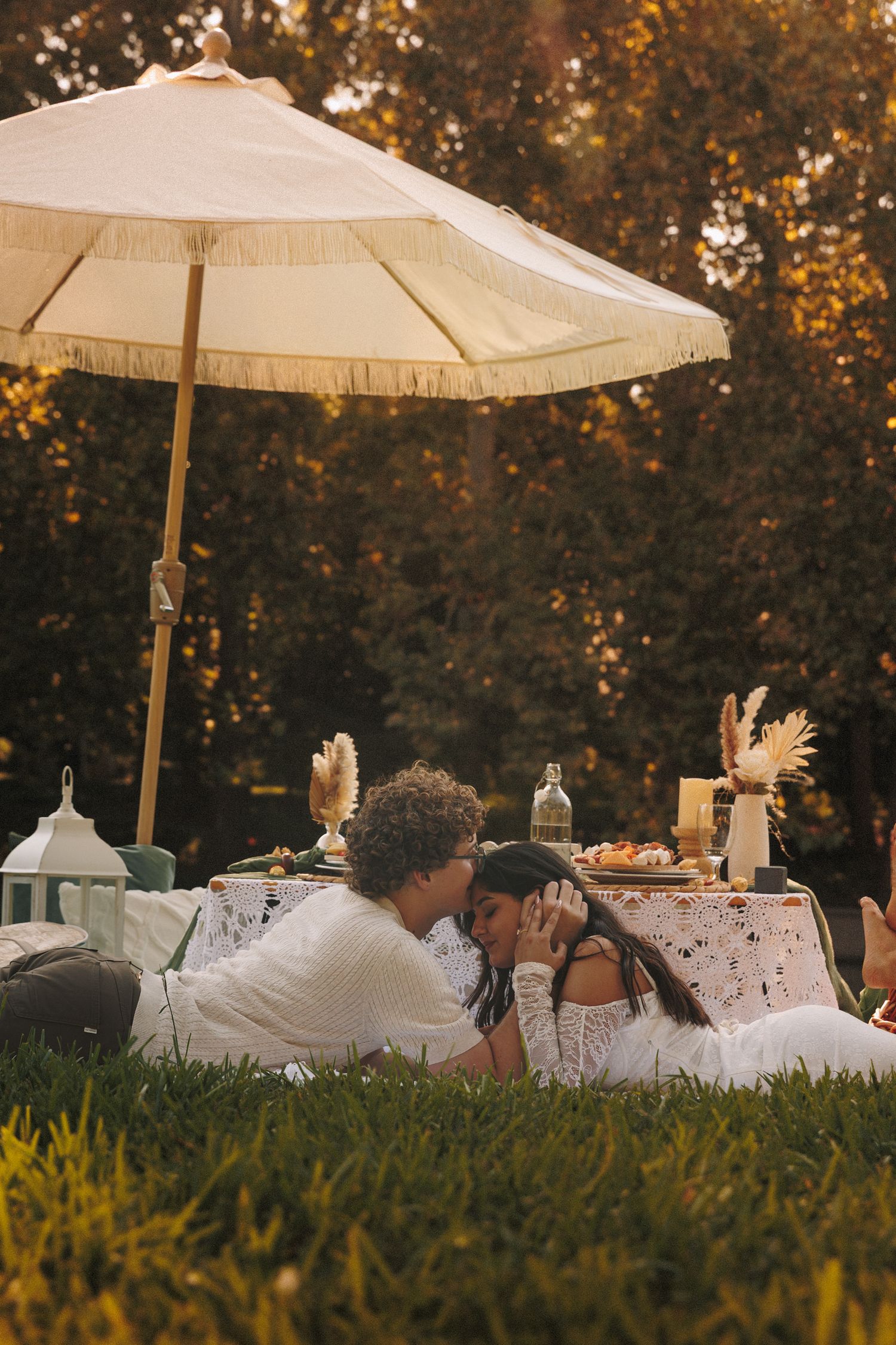 Cozy picnic spread with parasols, cushions and decorative elements laid out on grass at sunset.