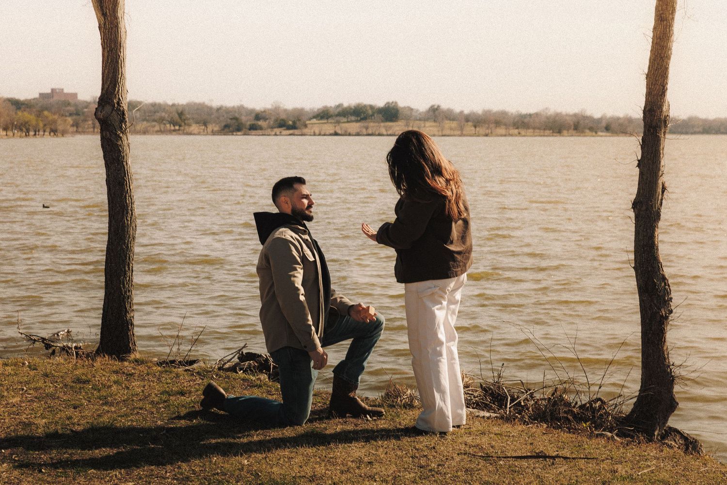 A romantic sunset silhouette scene with two people standing by a lake as golden light reflects on the water.