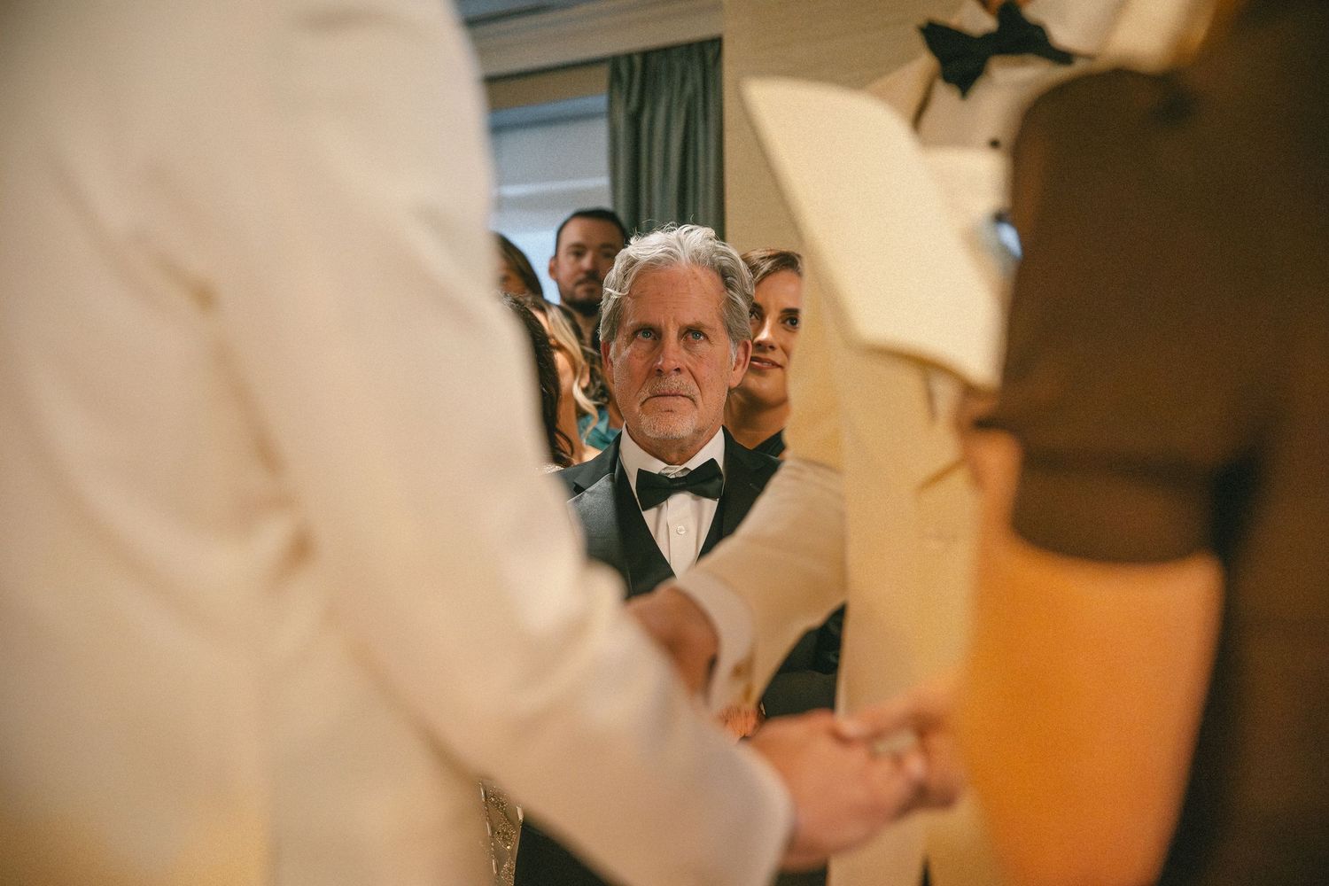 Emotional wedding guest in bow tie watches couple exchange vows during heartfelt ceremony.