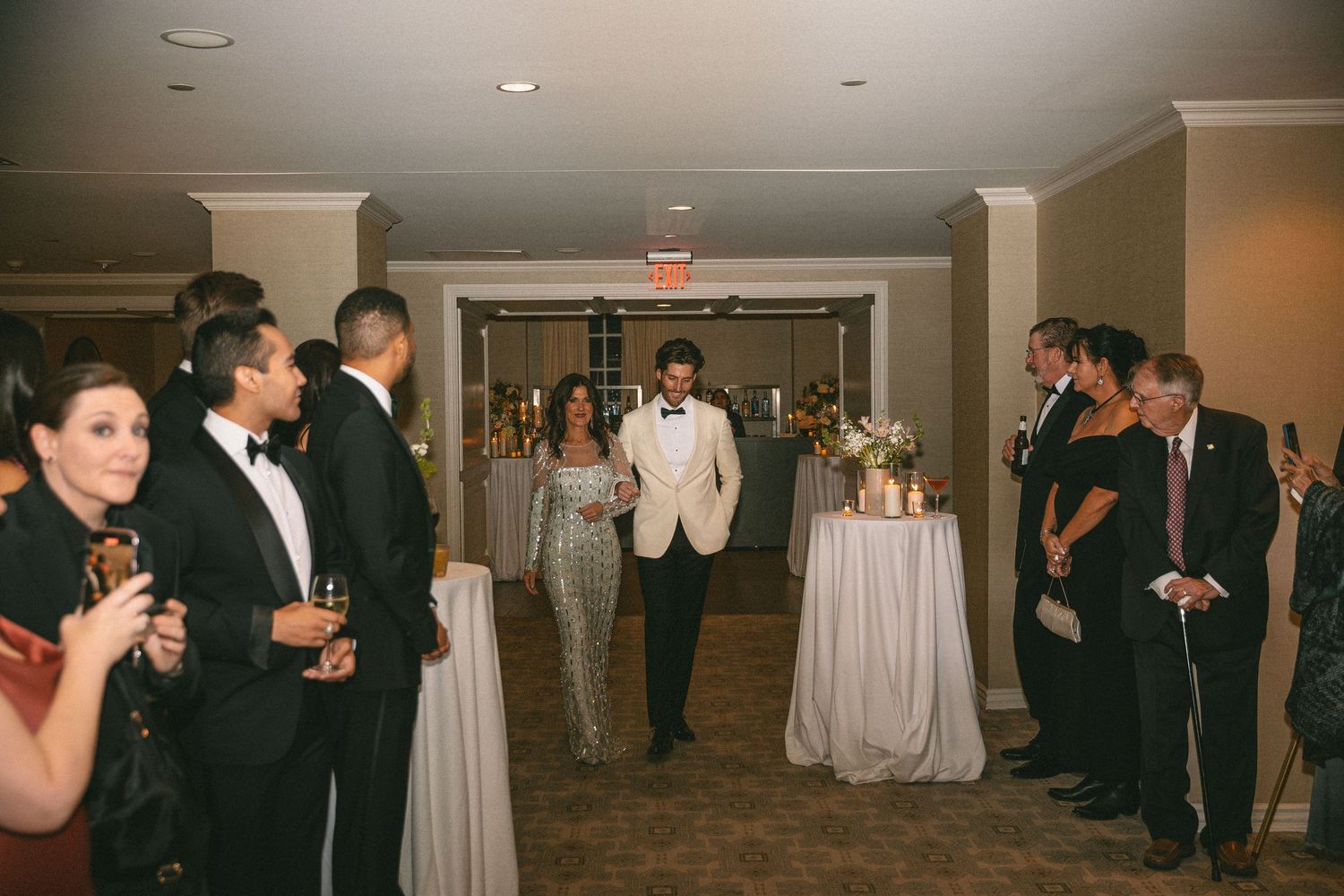 Two grooms make their grand entrance into an elegant wedding reception as guests applaud.