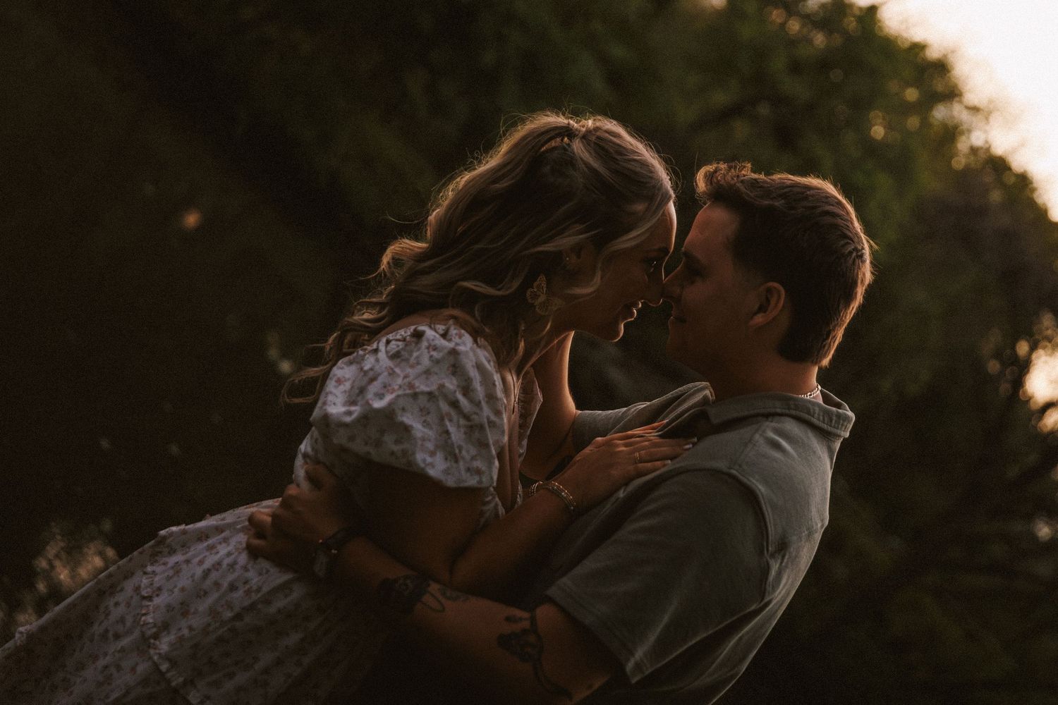 Couple embracing and leaning in for a kiss in warm golden sunset light.
