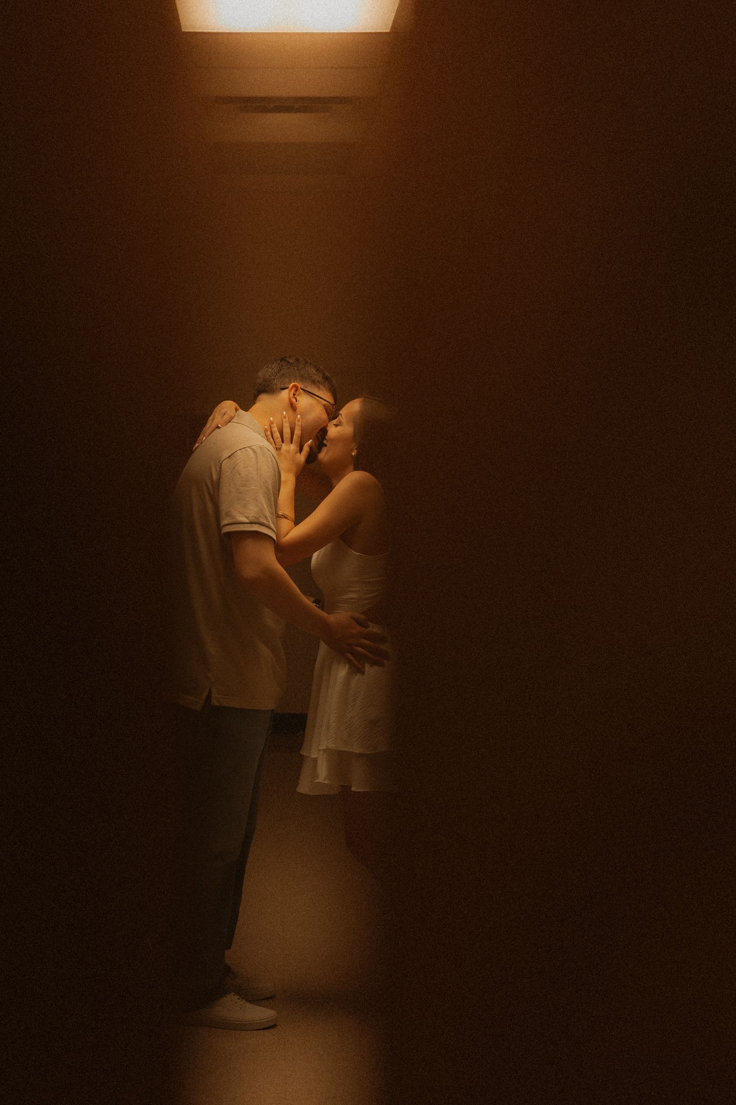Couple sharing a romantic moment in a narrow dimly lit corridor with warm golden light overhead.