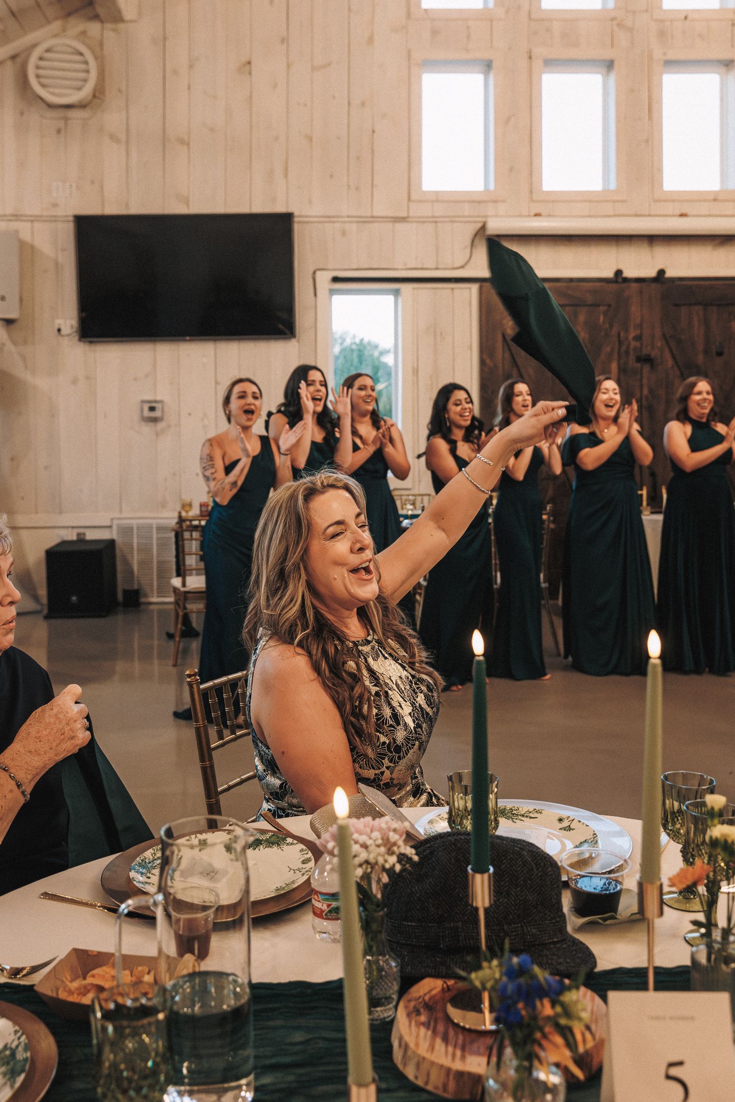 Excited wedding guest catching bouquet at reception while bridesmaids in emerald dresses cheer.