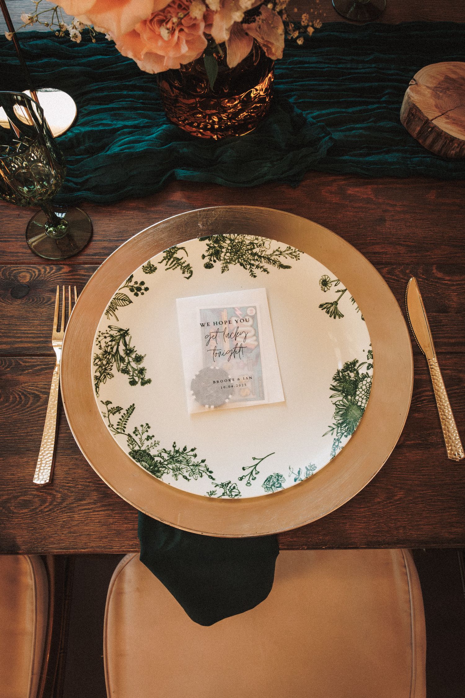 Elegant place setting with gold charger, green botanical plate, menu card, gold cutlery, and teal table runner.