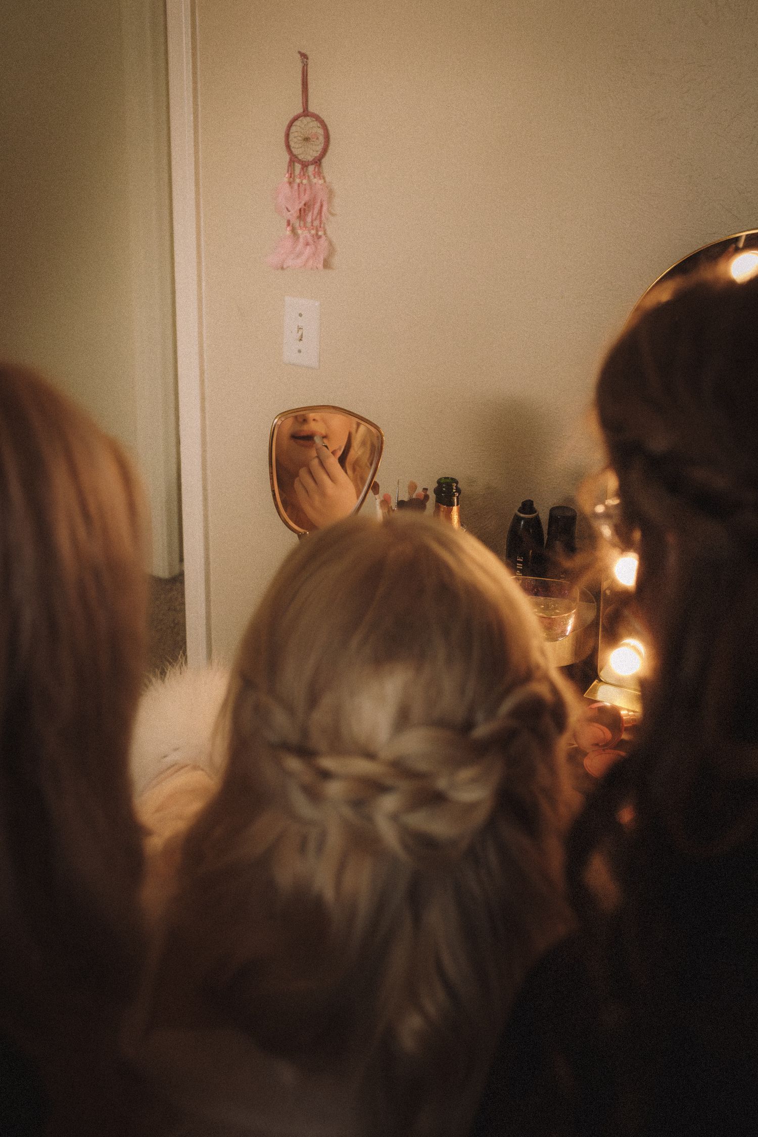 Girls with braided hairstyles getting ready in front of a mirror with a pink dreamcatcher on the wall.