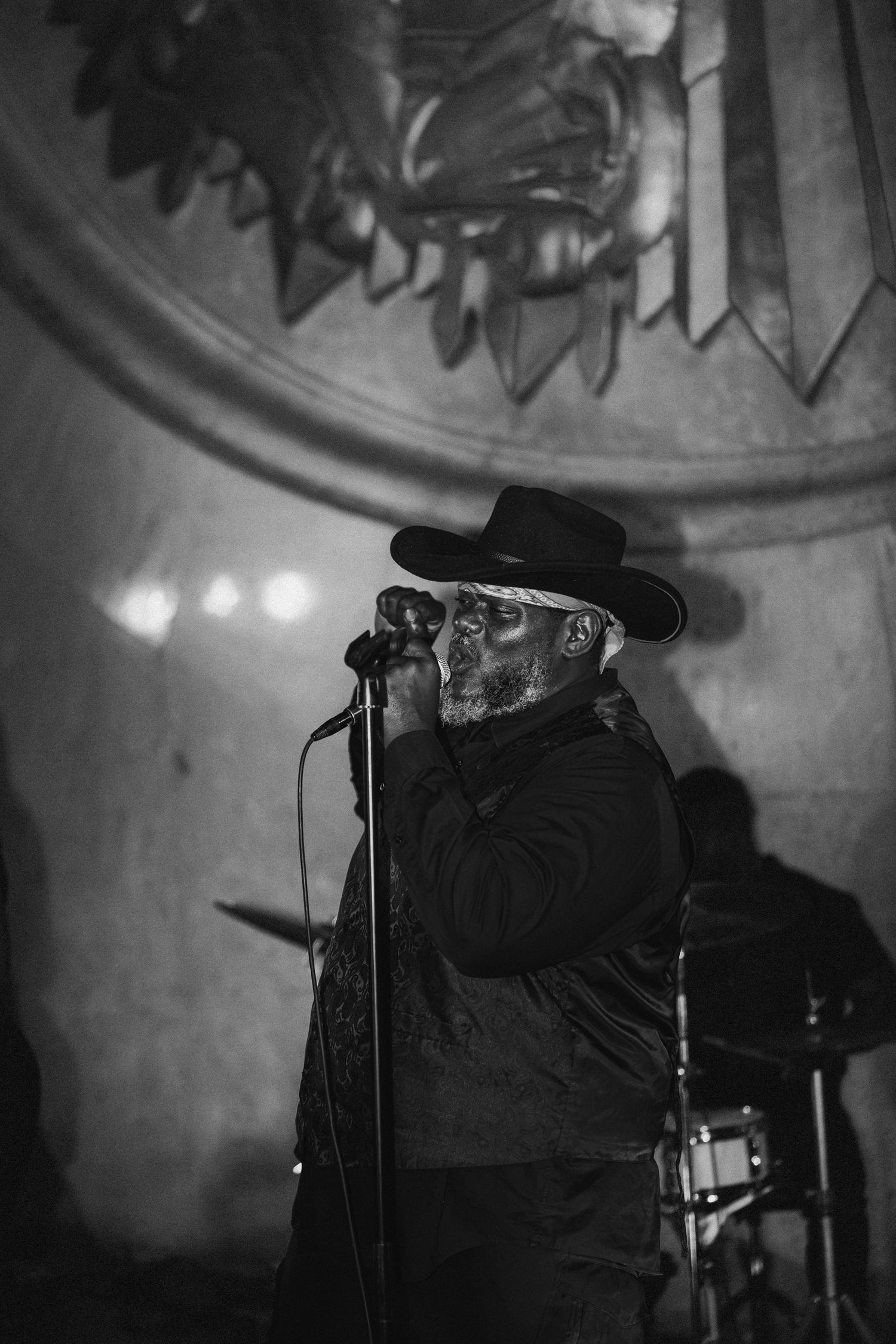 Black and white photo of male singer performing at microphone wearing cowboy hat at wedding.