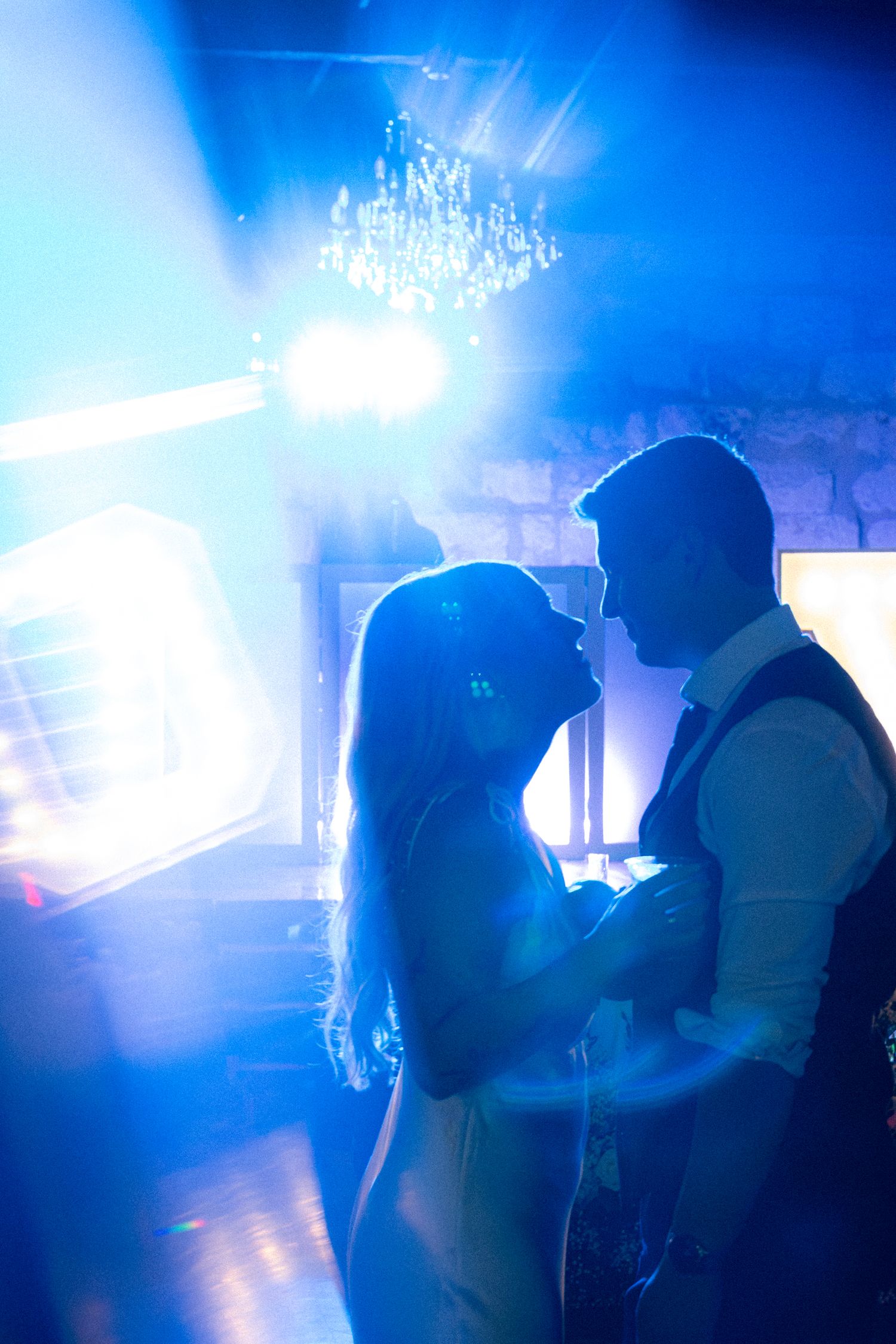 Bride and groom share romantic first dance silhouetted against dramatic blue stage lighting.