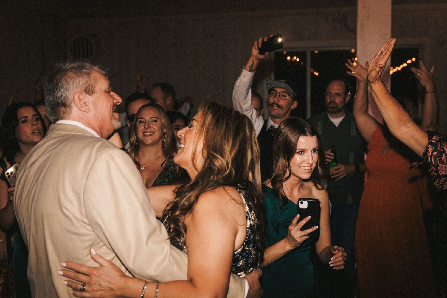 Guests dancing and celebrating joyfully at a lively wedding reception with sparklers and smiles.