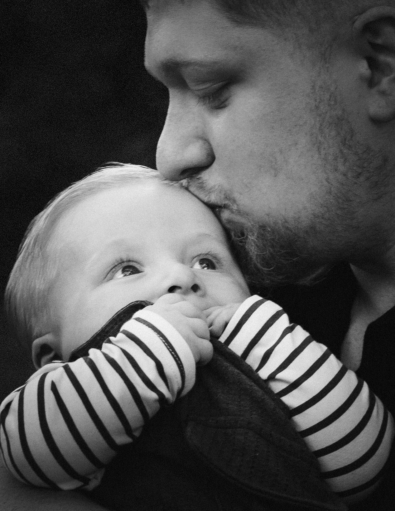 A black and white sequence showing someone in a striped sleeve softly touching and kissing a small infant.