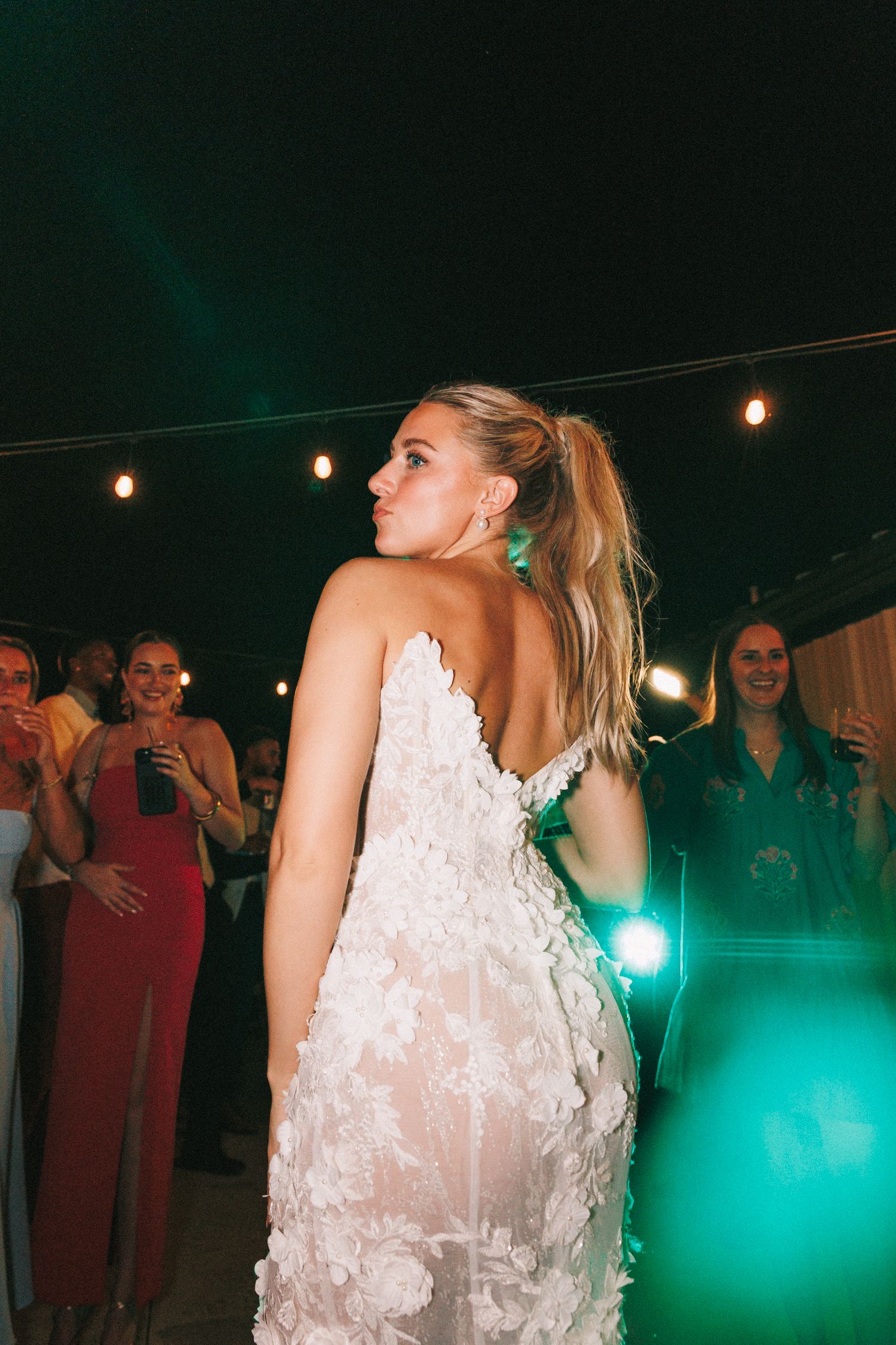 People dancing and celebrating at a wedding reception with string lights and turquoise lighting effects.