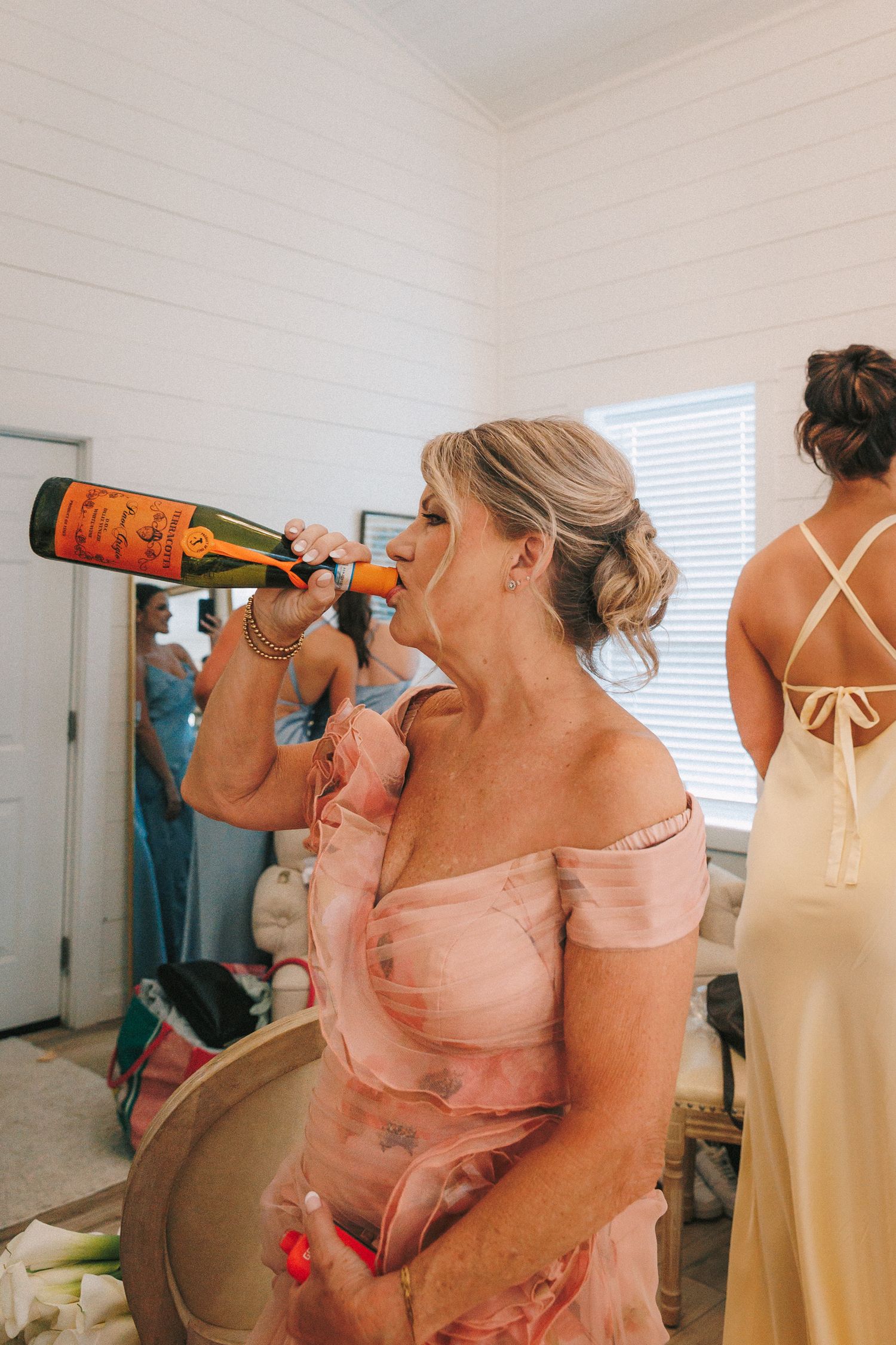 Bridesmaids in pastel dresses celebrate with drinks during pre-wedding preparations.