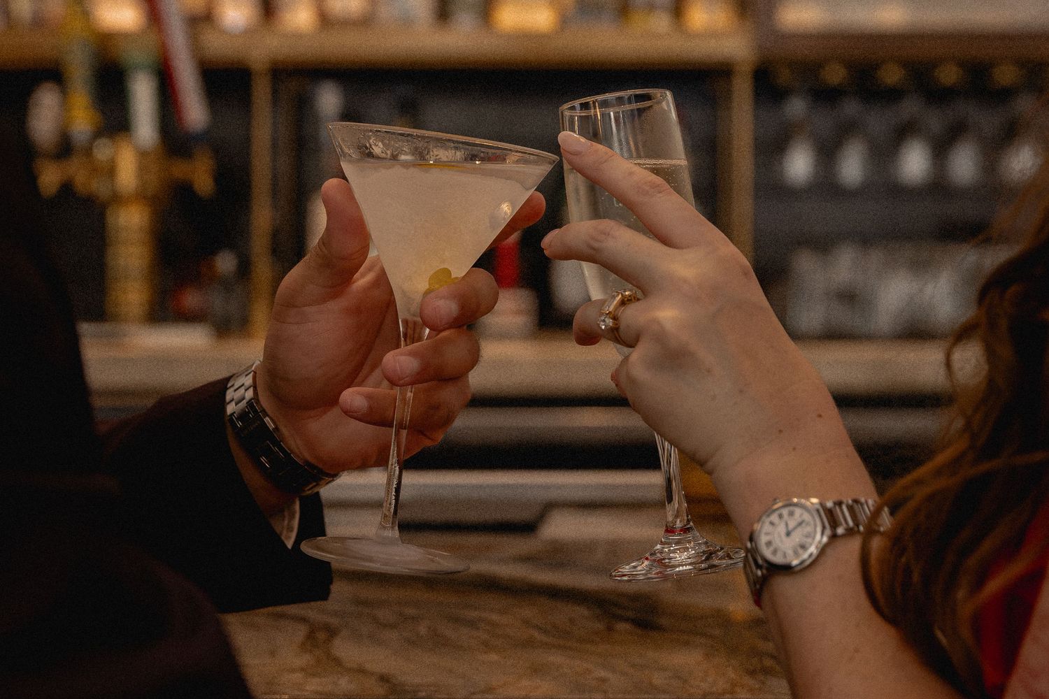 Two people toasting with elegant cocktails at a upscale bar, one holding a martini glass.