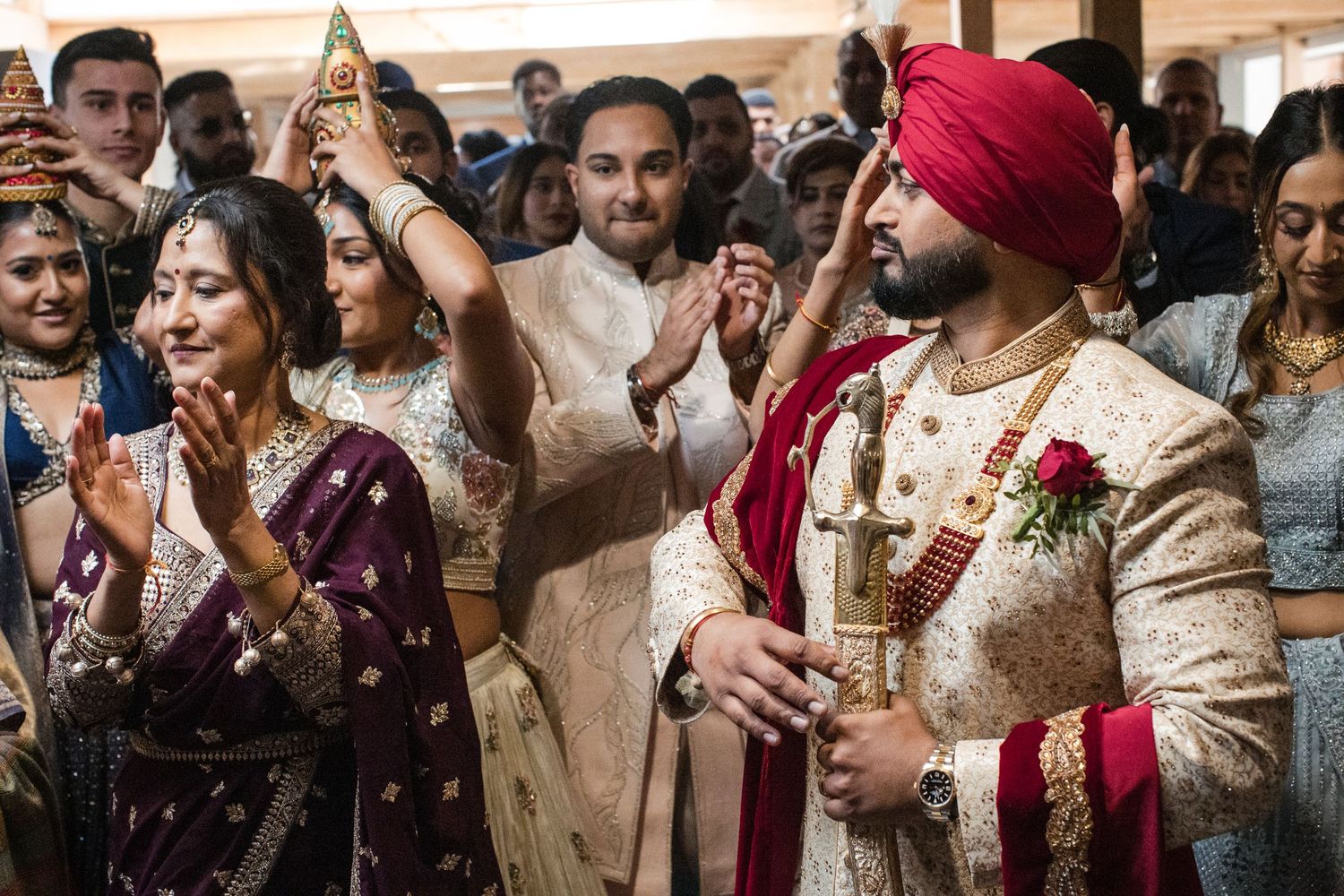 Sikh groom in red turban and sherwani celebrates with wedding guests during traditional Indian ceremony.