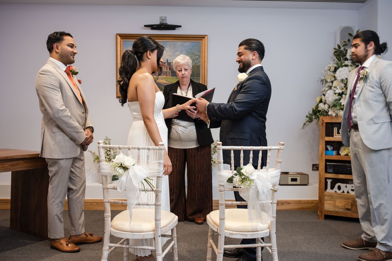 Couple exchanges vows before officiant at intimate wedding ceremony with white floral decorations.