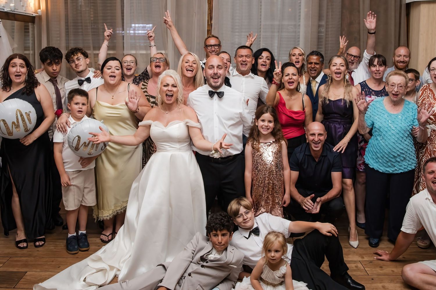 Bride and groom celebrate with wedding guests in a joyful group photo at their reception.