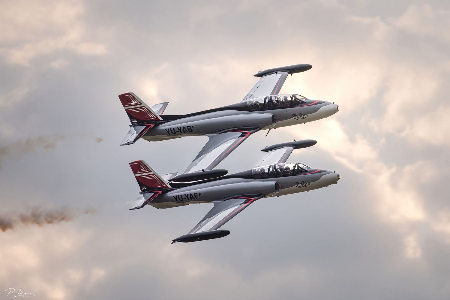 Two silver jet aircraft perform a synchronized formation flight maneuver against a dramatic cloudy sky.