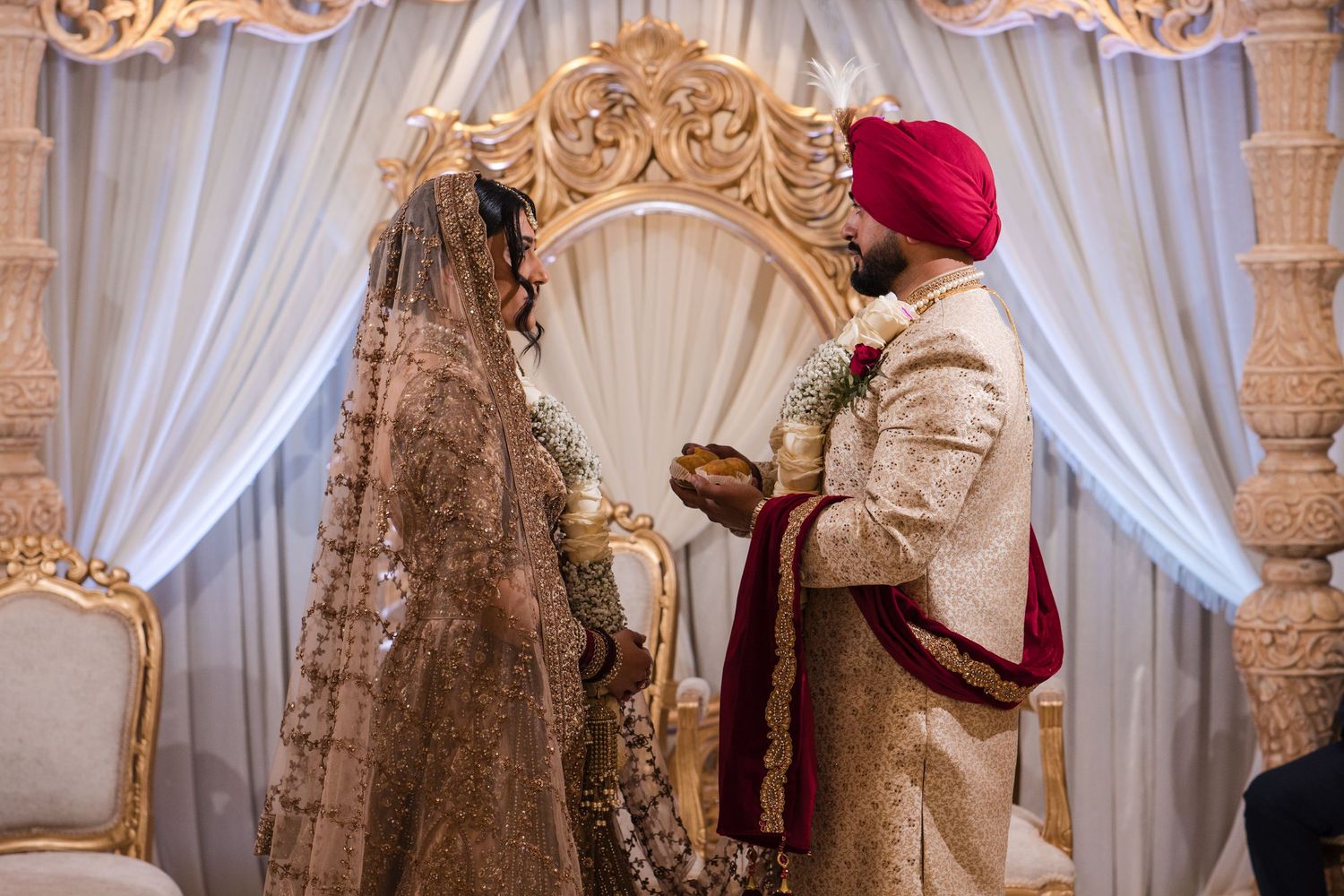 Sikh bride and groom exchanging vows at ornate gold mandap during traditional Indian wedding ceremony.