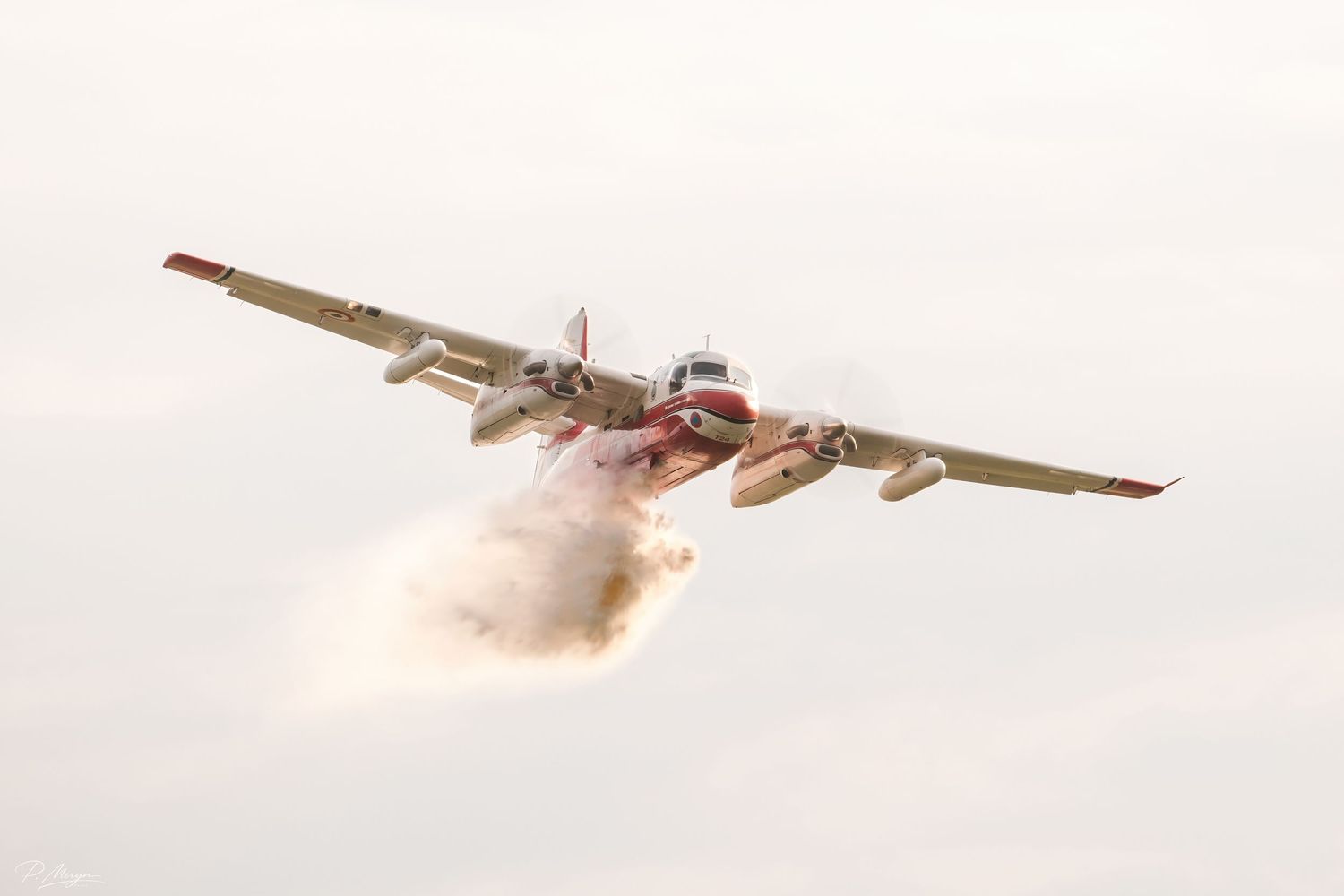 A red and white firefighting air tanker aircraft dropping water or retardant during an aerial firefighting operation.