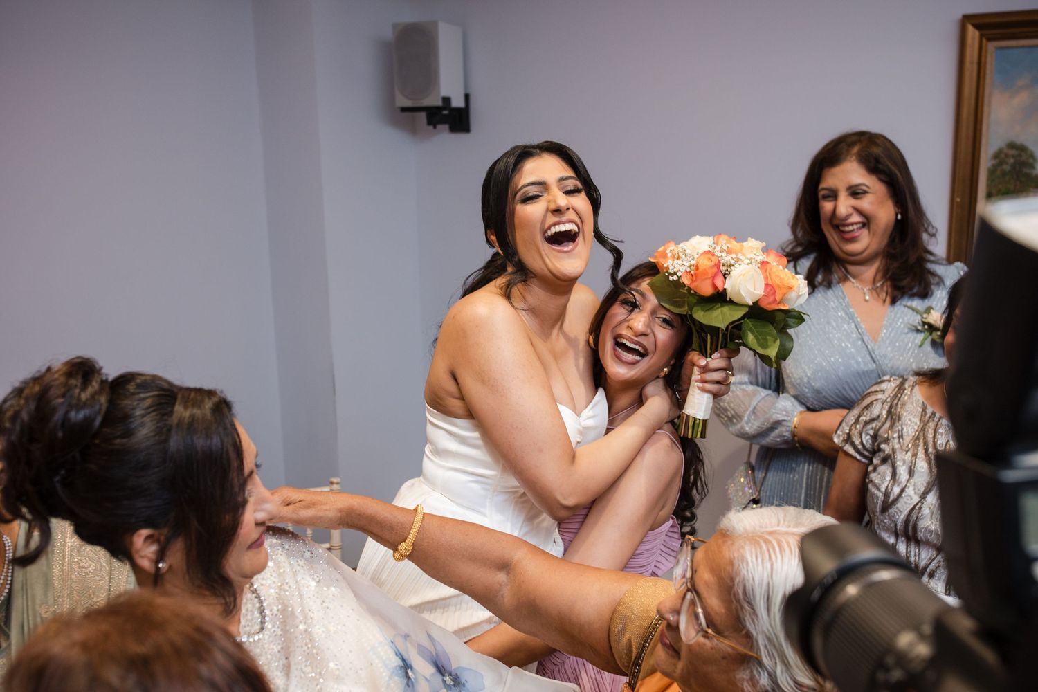 Joyful bride in white dress laughing with guests while holding peach bridal bouquet.