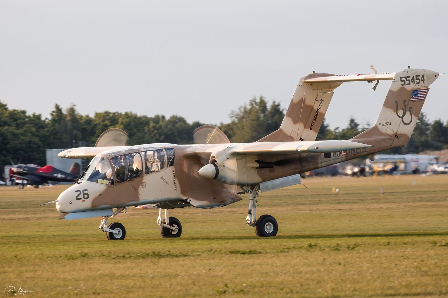 A US Marines OV-10 Bronco in desert camouflage scheme with number 26 taxiing on a grass airfield.