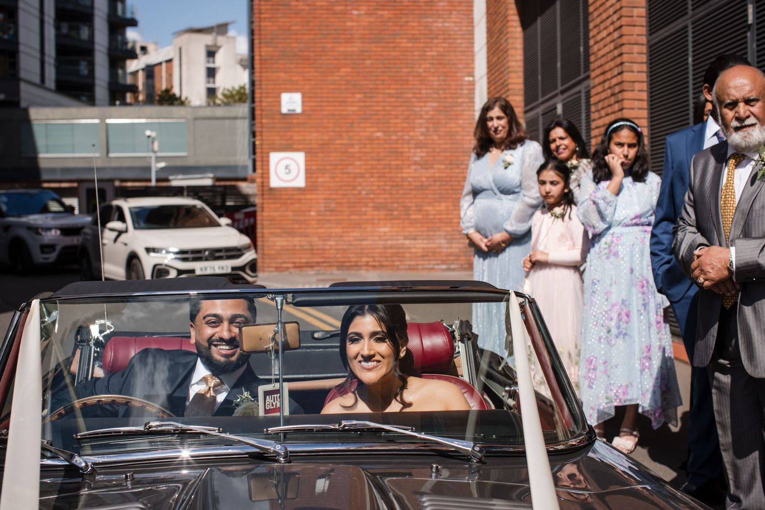 Bride arriving in a convertible car with wedding guests watching