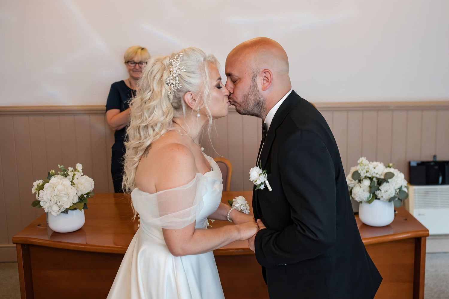 Newlywed couple shares their first kiss at the altar during intimate wedding ceremony with officiant in background.