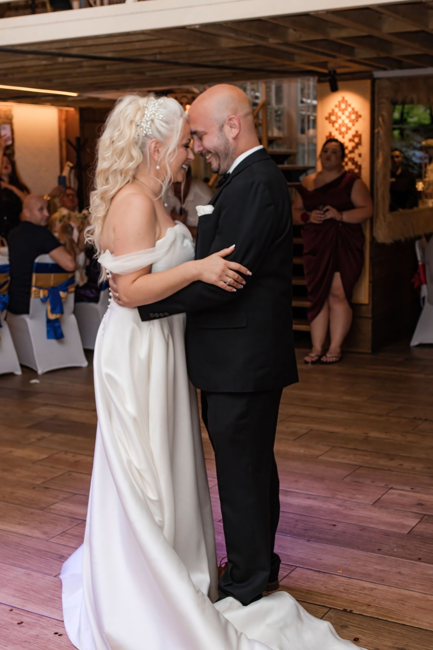 Bride and groom share their first dance, smiling intimately in a rustic wedding reception venue.