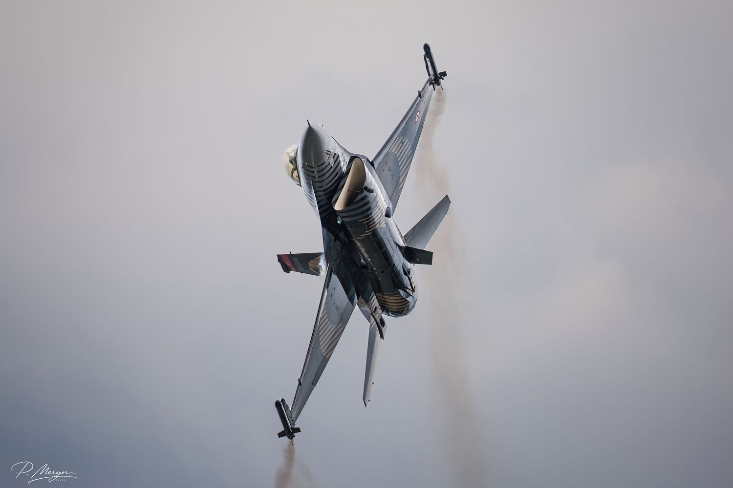 F-16 Fighting Falcon jet in steep climb with smoke trail at airshow display.