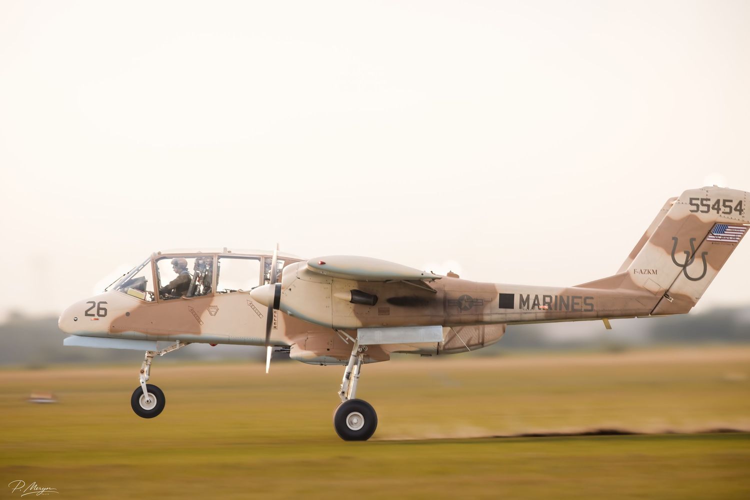 A US Marines OV-10 Bronco aircraft in desert camouflage with tail number 55454 taxiing on a grass runway.