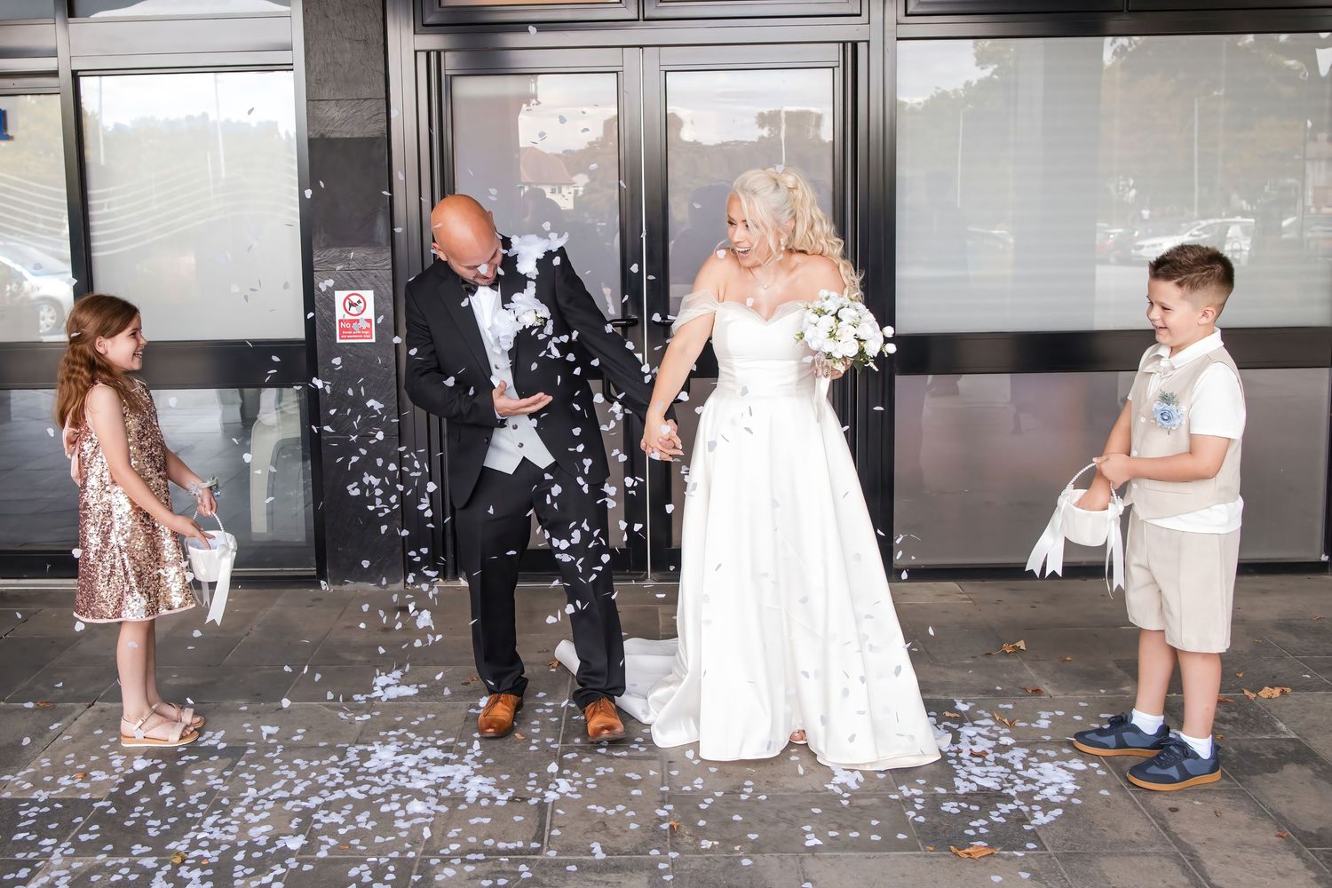 Bride and groom are showered with white confetti by two children outside after their ceremony.