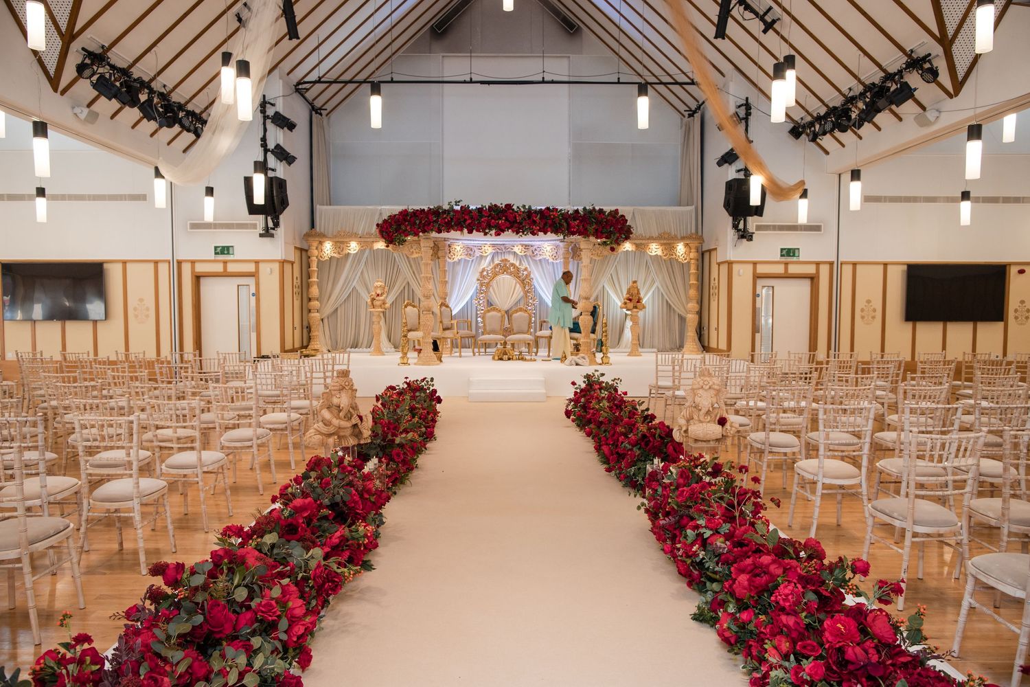 Elegant wedding ceremony venue with red rose aisle arrangements, chiavari chairs, and ornate gold mandap backdrop.