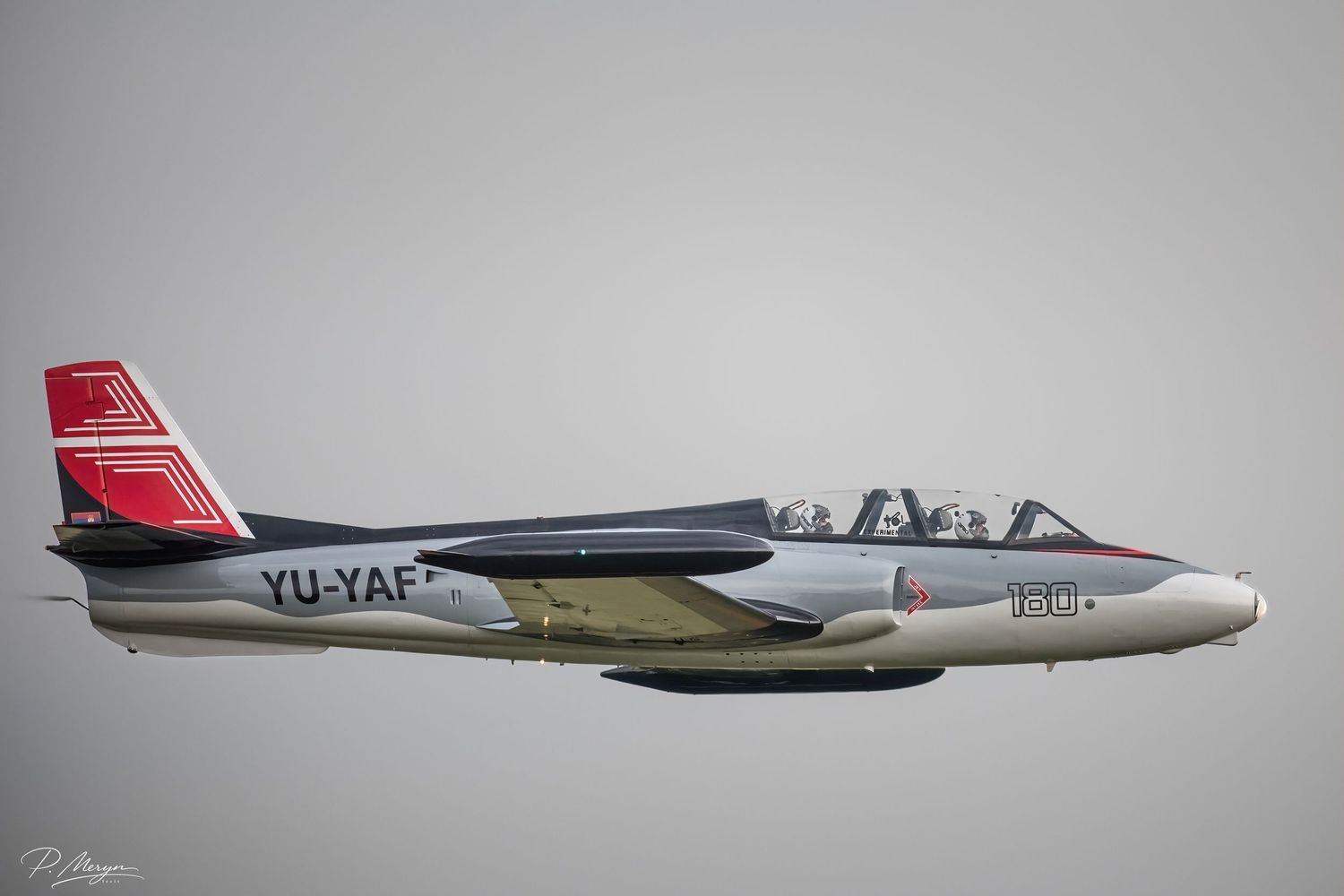 A YU-YAF jet trainer aircraft flies low against an overcast sky at an airshow.