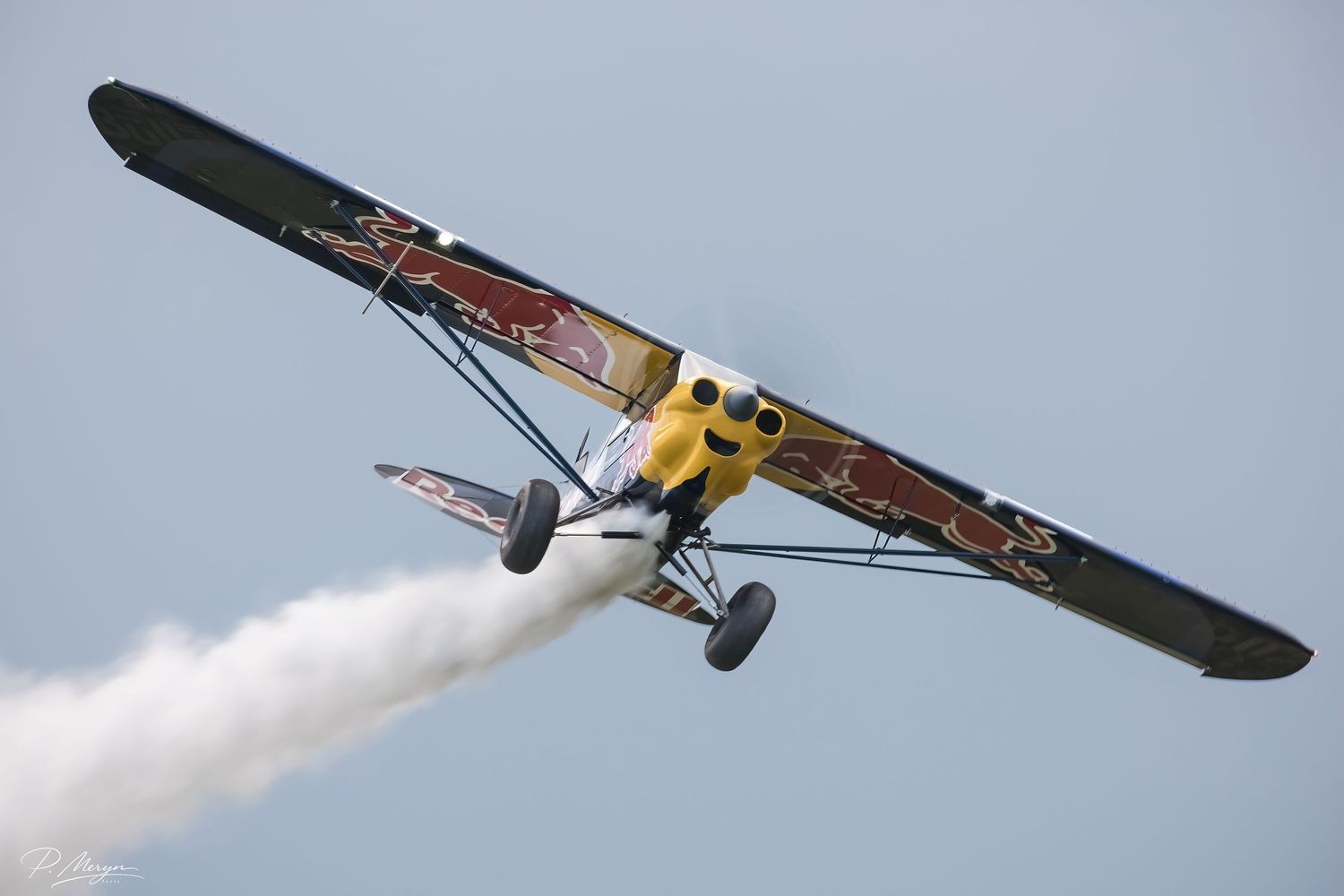 A yellow and red biplane performs aerobatics with white smoke trail at an airshow.