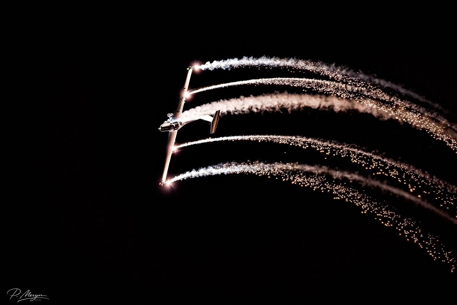 Aerobatic aircraft leaving glowing smoke trails against black night sky at airshow.