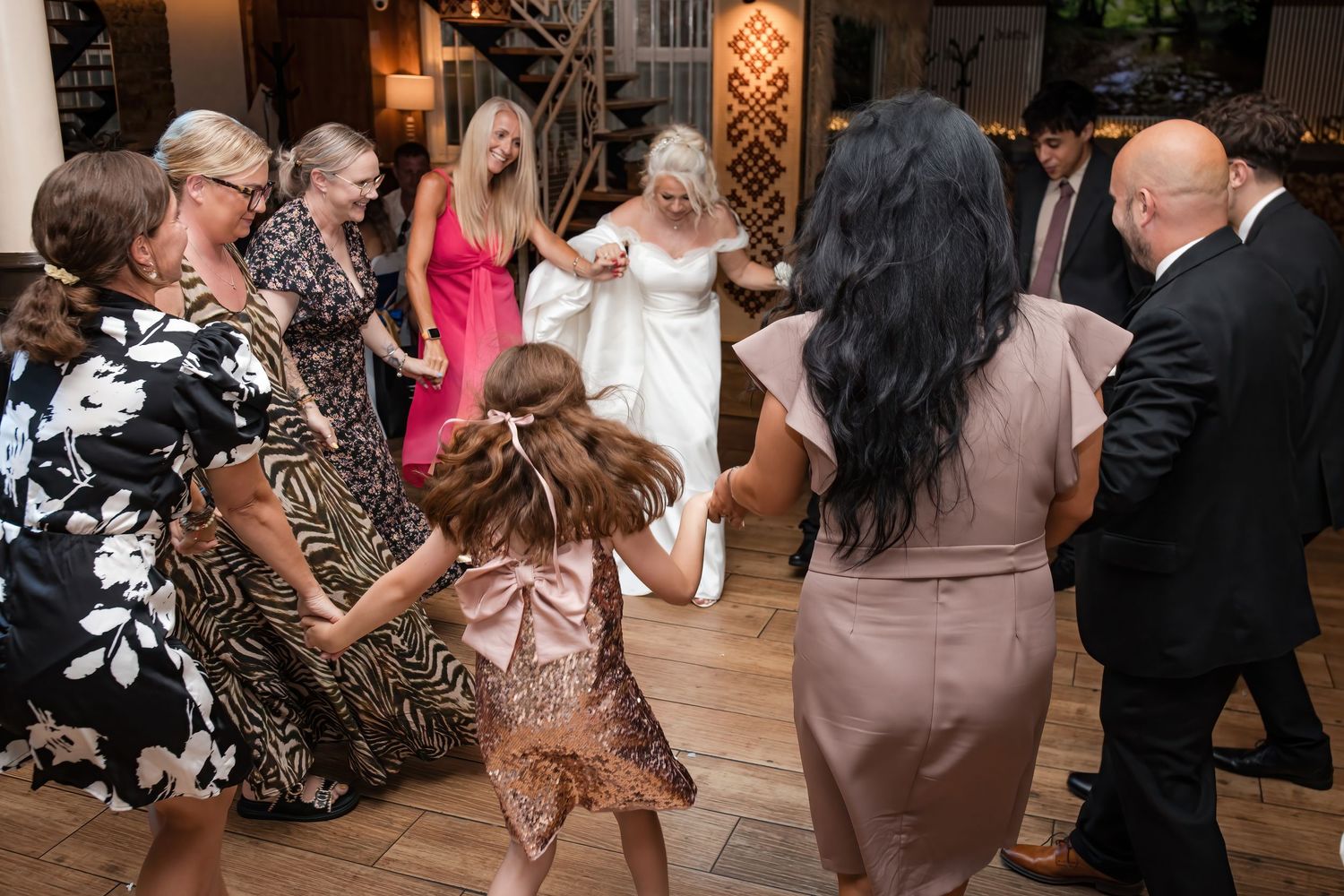 Wedding guests form a circle dancing with the bride on the wooden dance floor at the reception.