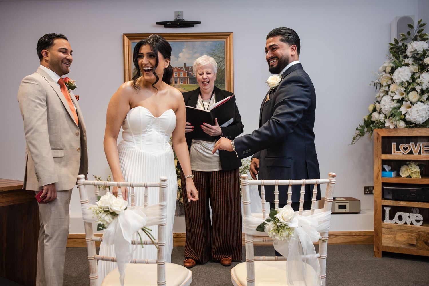 Joyful bride and groom laugh while exchanging vows at intimate wedding ceremony with white decor.