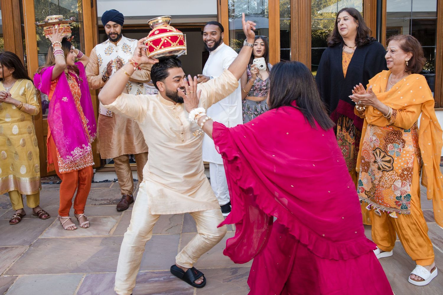 Guests in colorful traditional Indian attire dance and celebrate during a lively wedding ceremony outdoors.