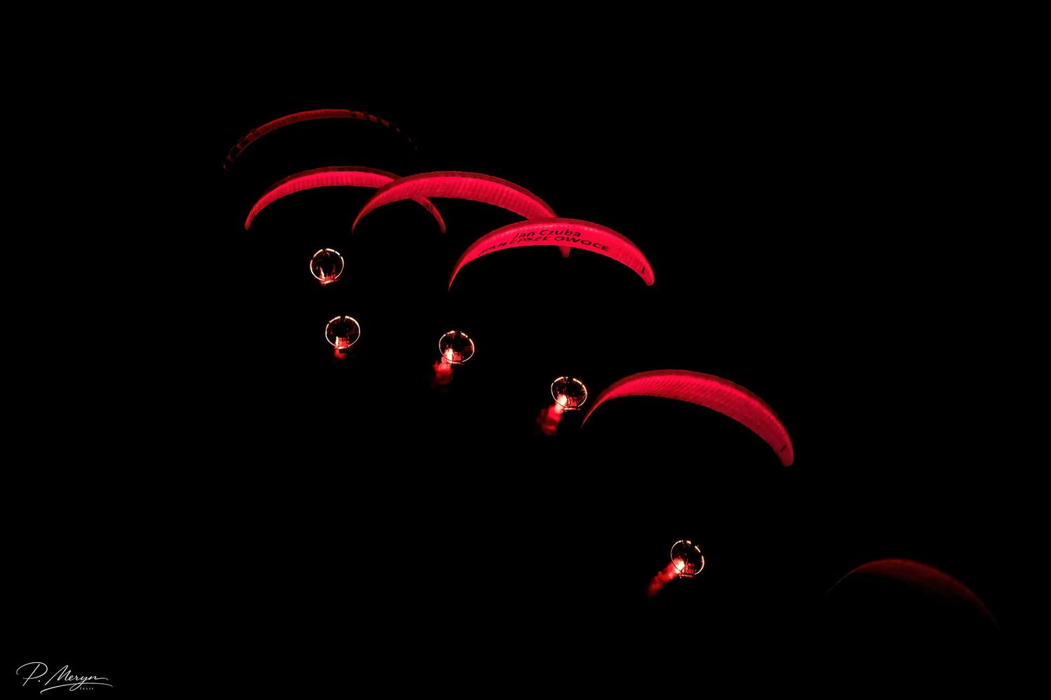 Red parachutes with lights glowing against dark night sky during dramatic nighttime airshow.