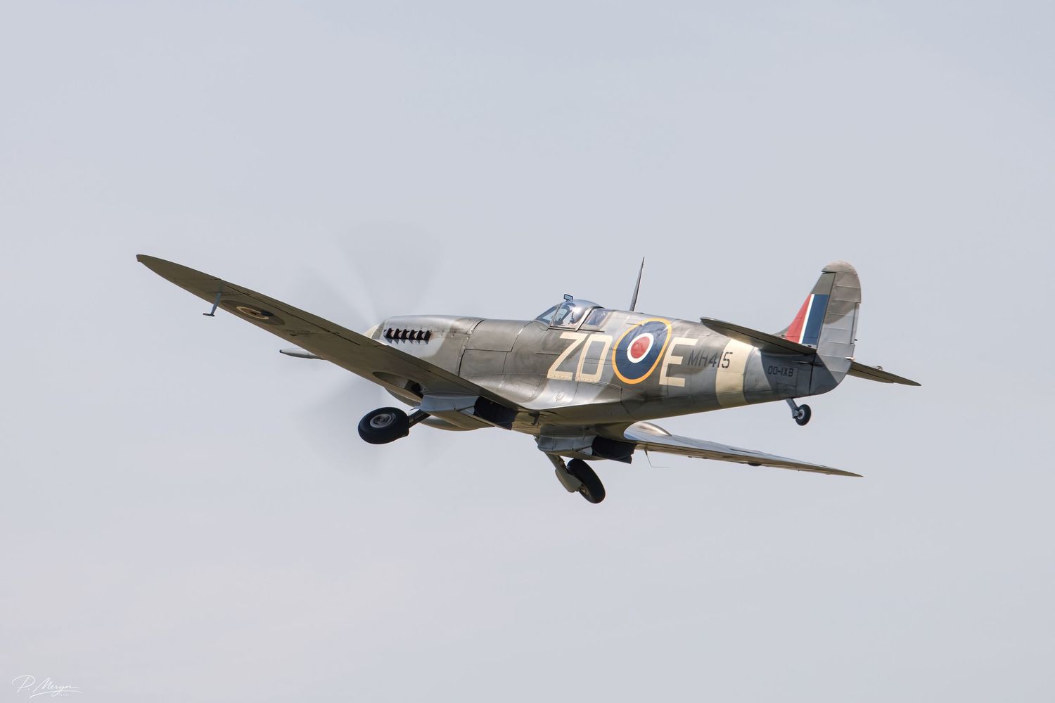 Classic WWII Supermarine Spitfire with RAF markings ZL-E in flight against overcast sky.