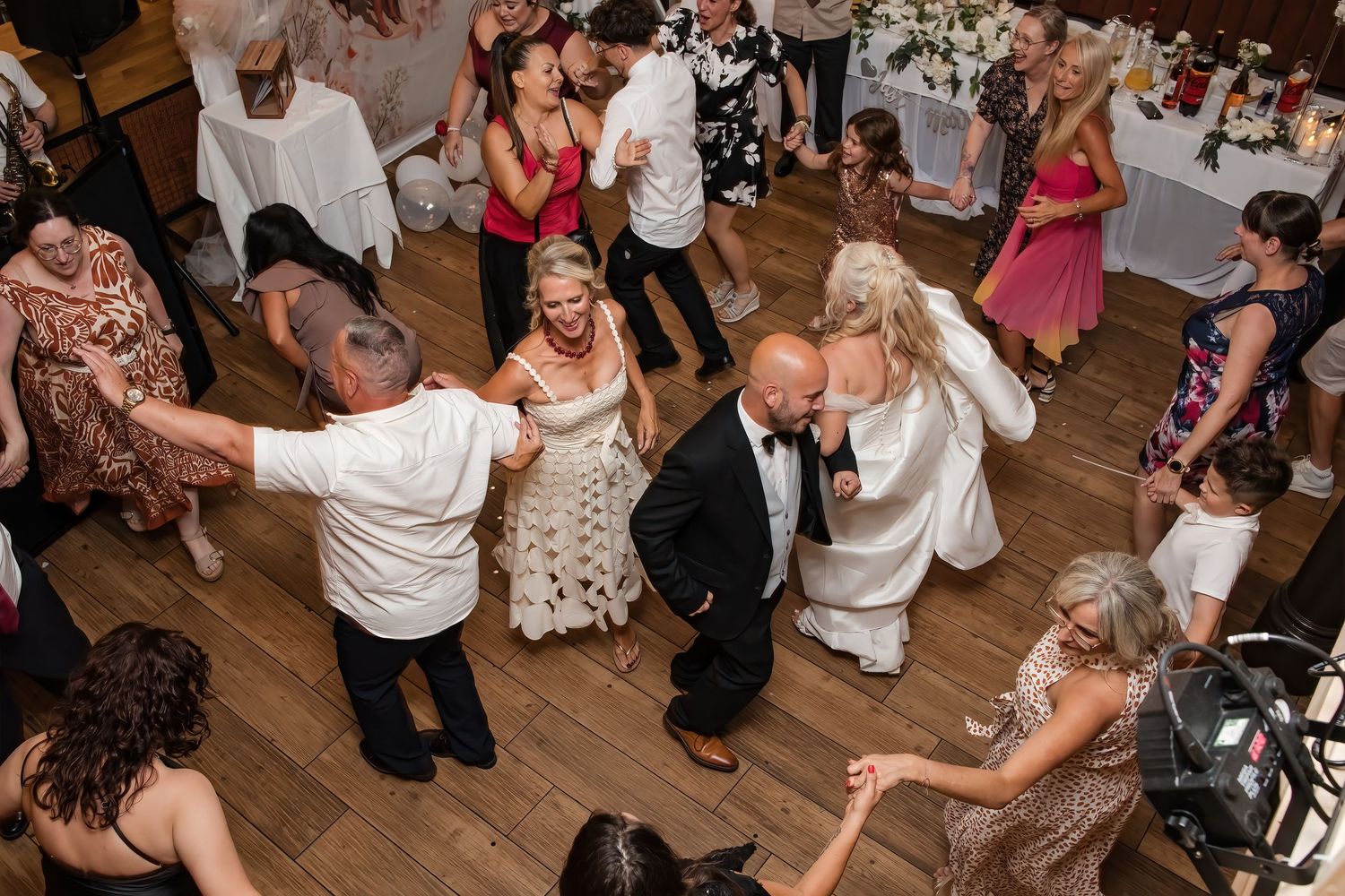 Aerial view of bride, groom and guests enjoying lively group dancing at wedding reception celebration.