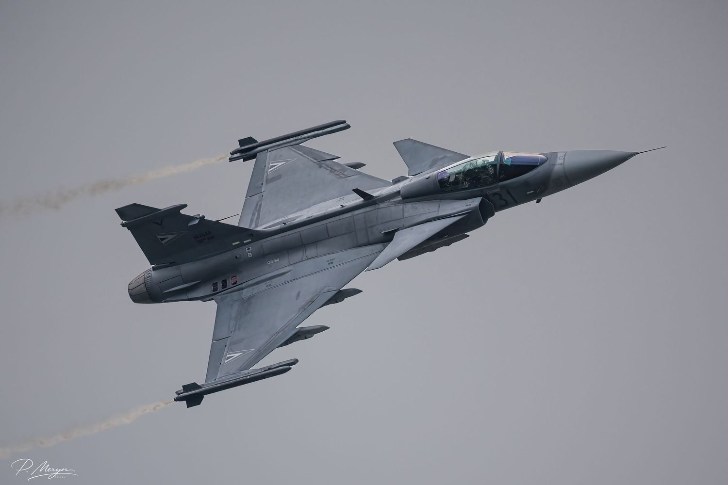 Saab JAS 39 Gripen fighter jet performing aerobatic maneuver at airshow against overcast sky.