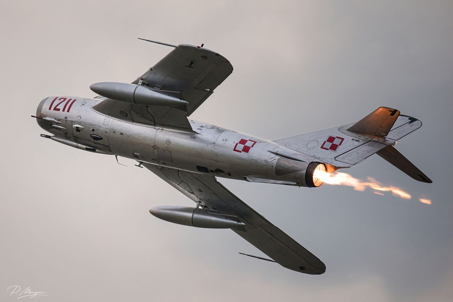 Polish MiG-15 jet fighter numbered 1211 firing afterburner during dramatic airshow display against cloudy sky.